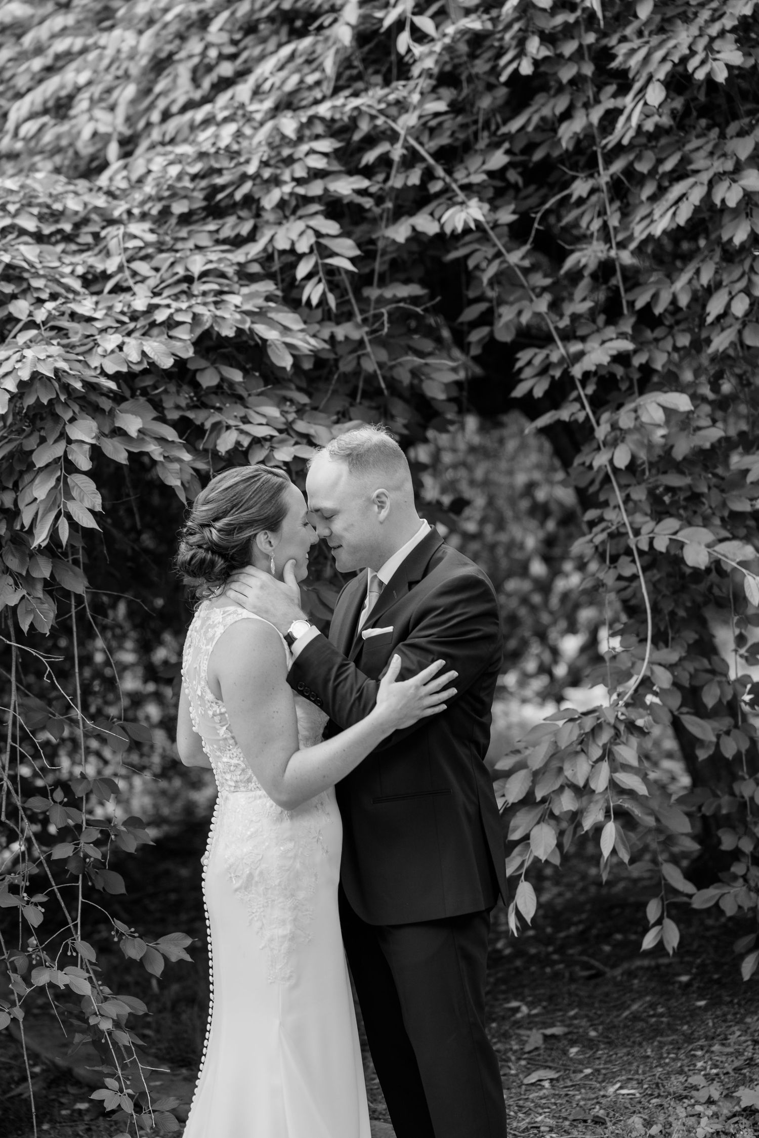 Black and white portrait of bride and groom sharing a romantic moment under hanging vines.