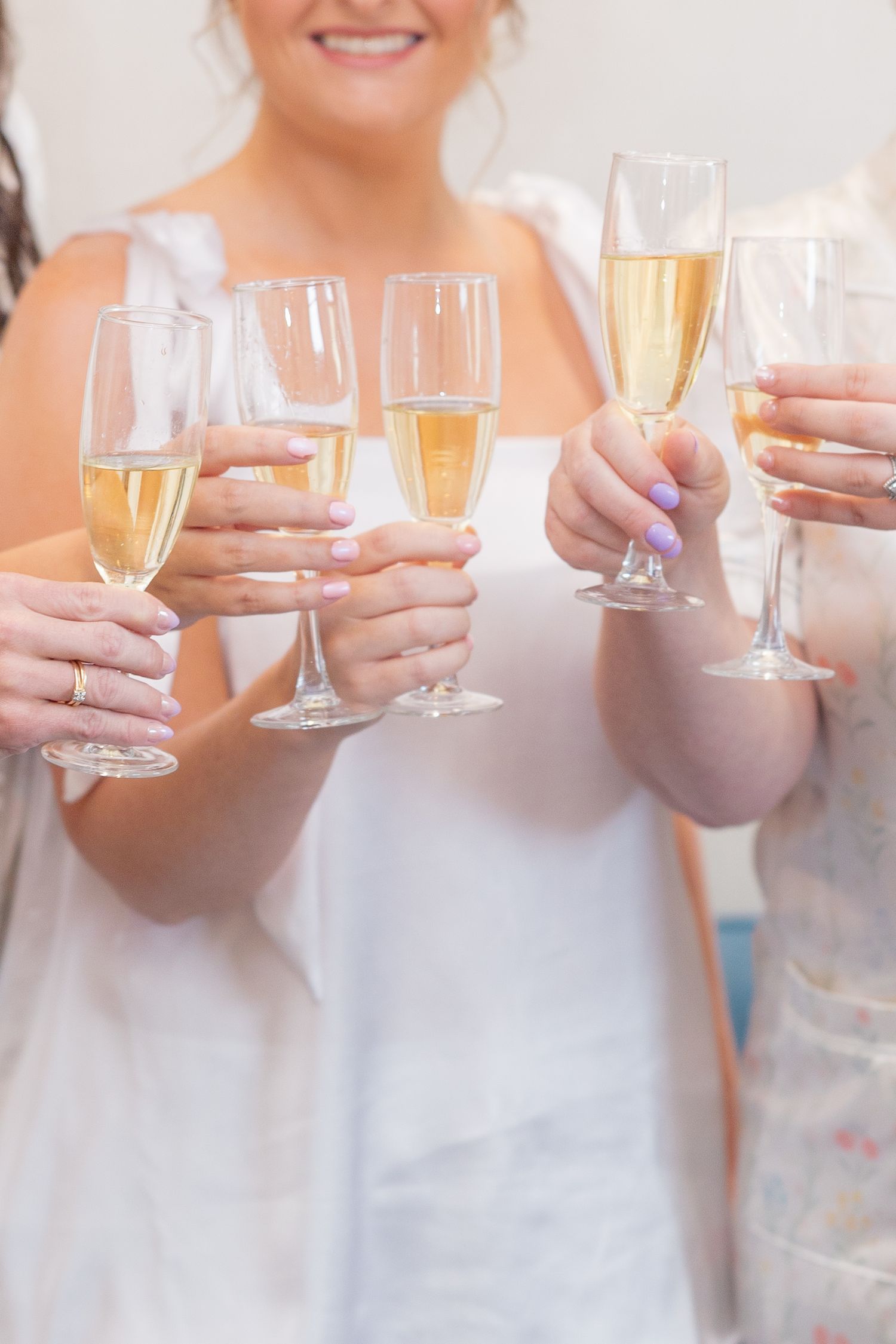Group of women in white dresses toasting with champagne flutes at a celebratory wedding event.