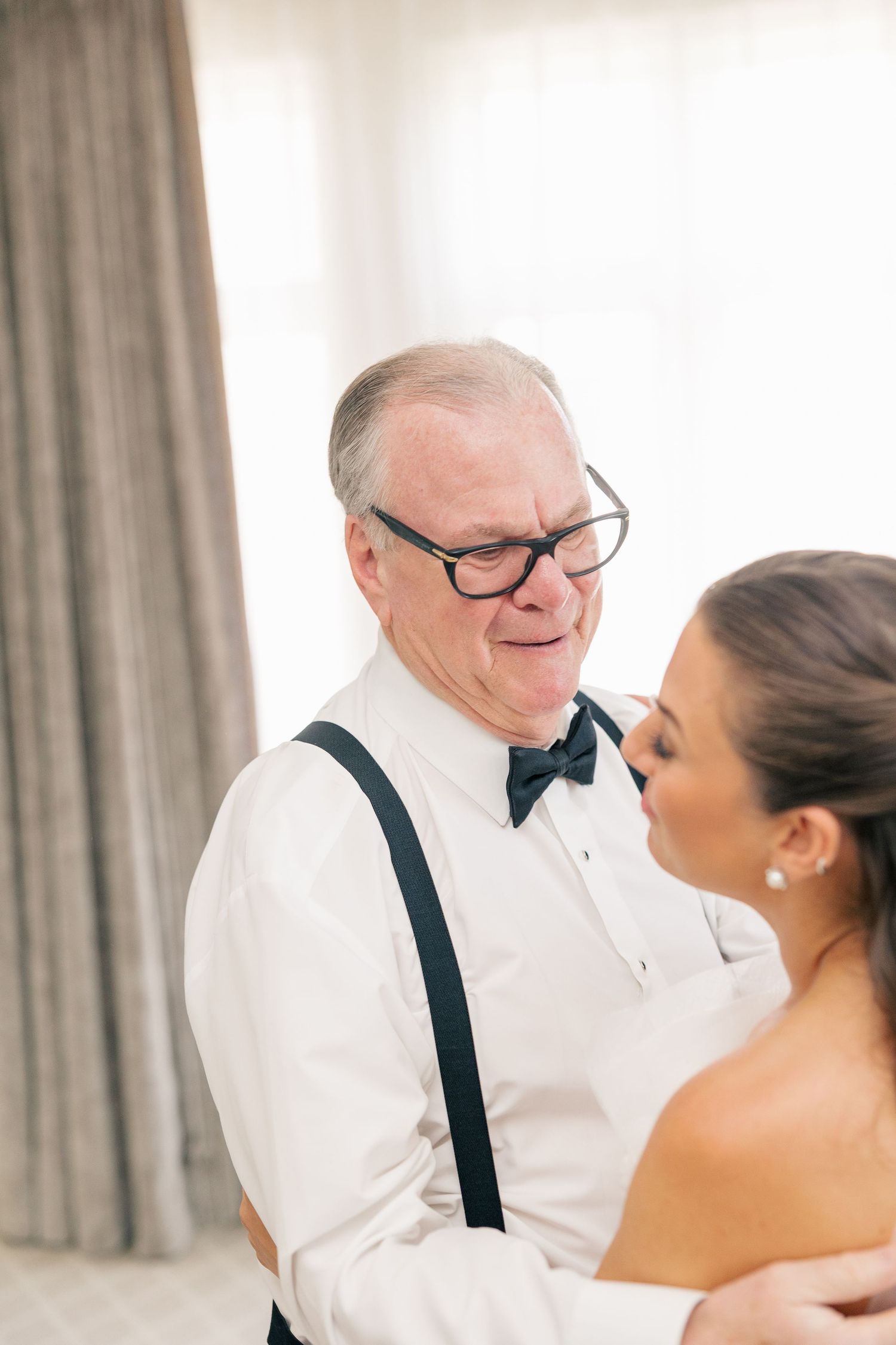 Emotional father in bow tie and suspenders embraces his daughter on her wedding day.