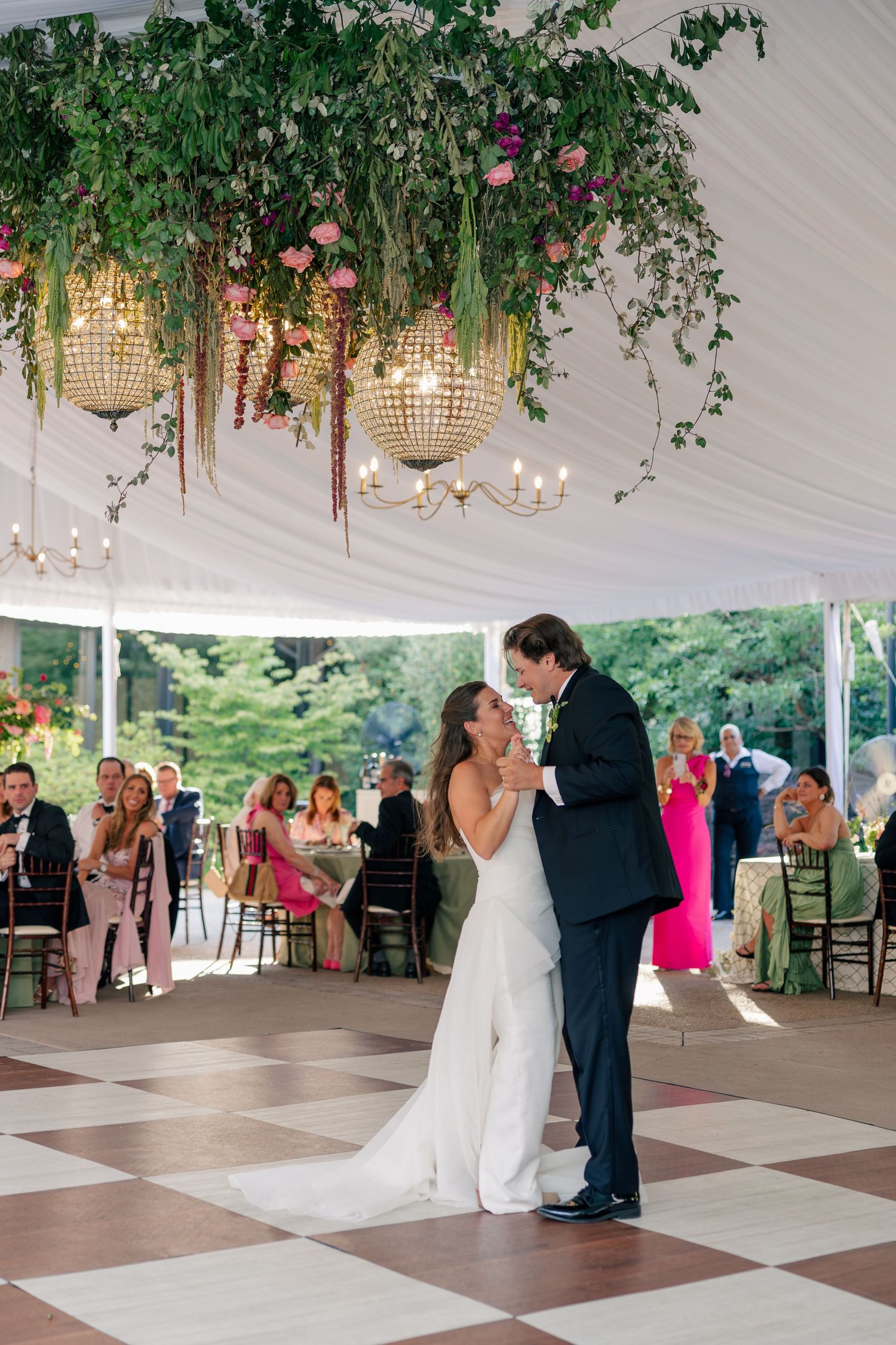 Couple shares romantic first dance kiss under cascading floral chandeliers in tented reception.