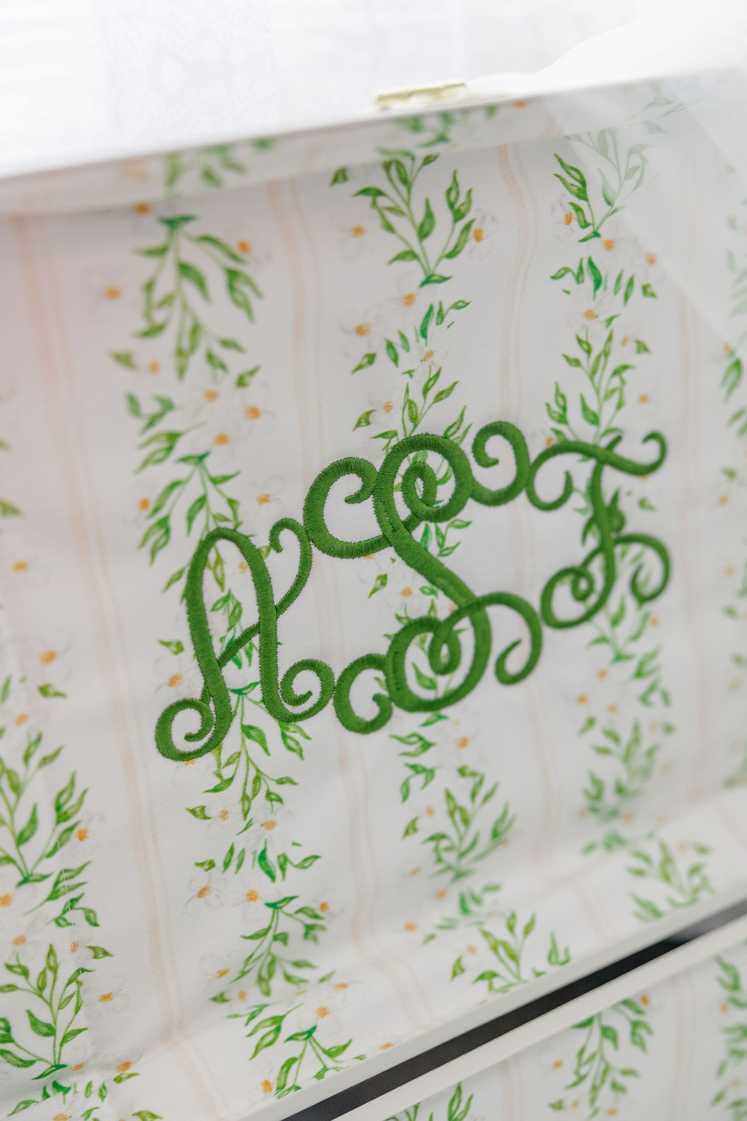 Elegant white wedding box with green floral pattern and ornate monogram embroidery detail.