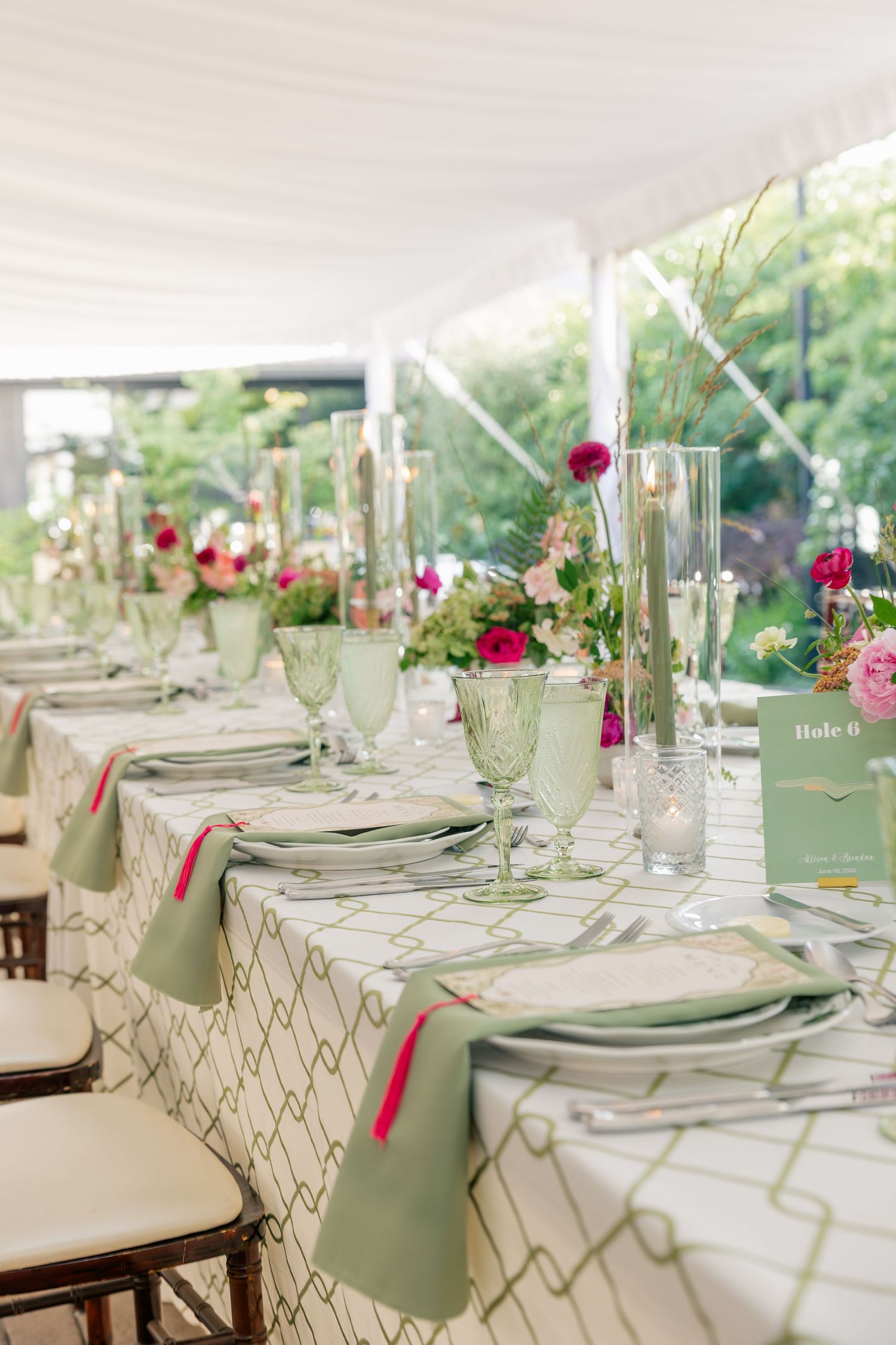 Elegant wedding reception table with green patterned linens, pink floral centerpieces, and green goblets.