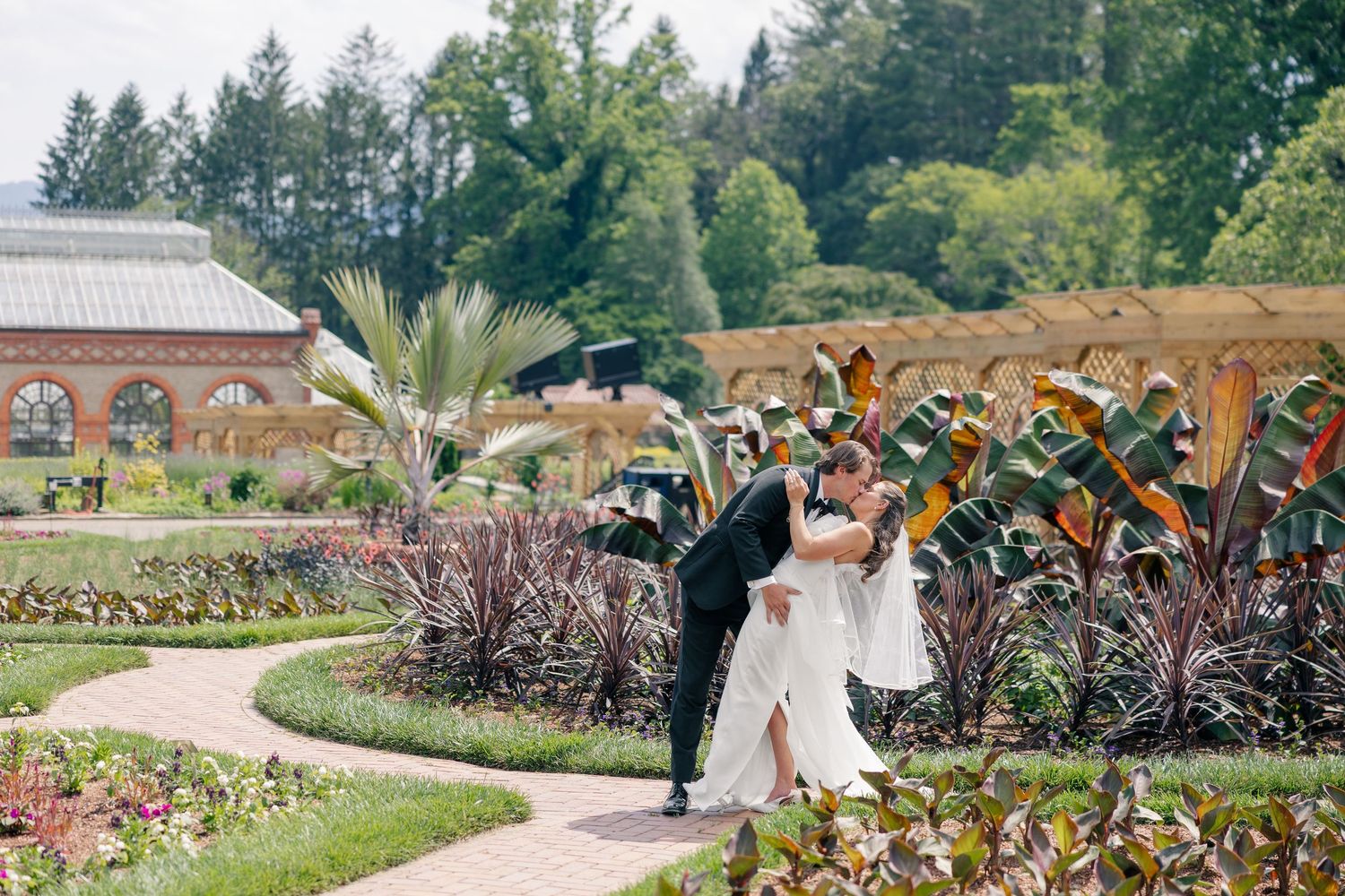 Bride and groom sharing romantic dip kiss in lush botanical garden with tropical plants.