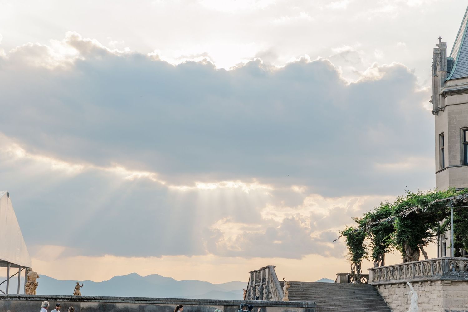 Sunbeams break through clouds over a mountain landscape with architectural details in view.