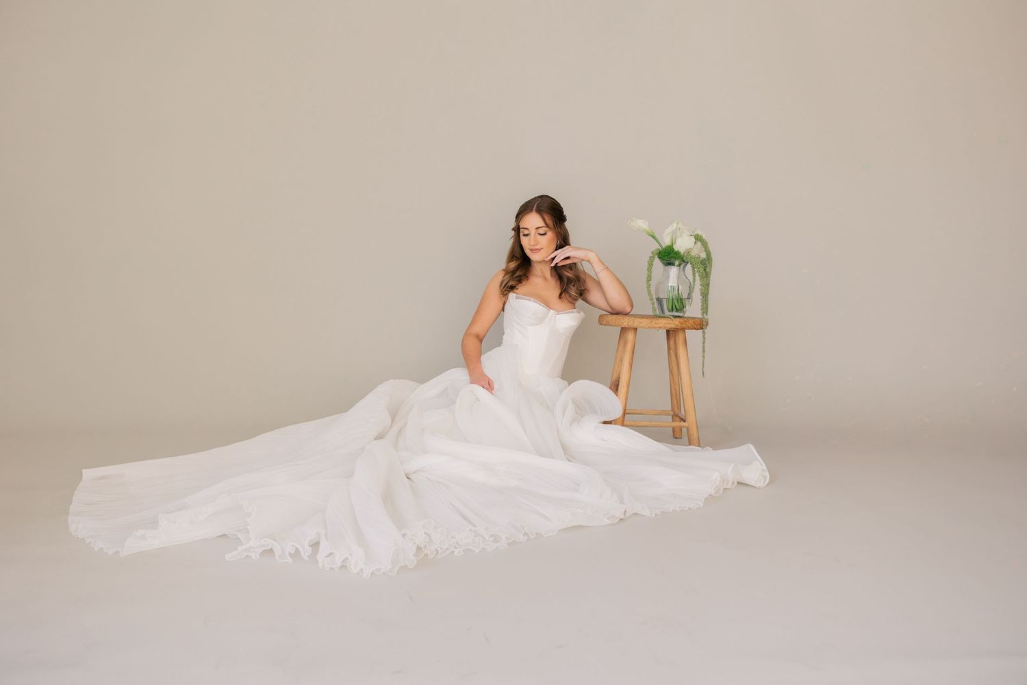 A bride in a white wedding dress poses gracefully on a backdrop while holding a delicate floral bouquet.