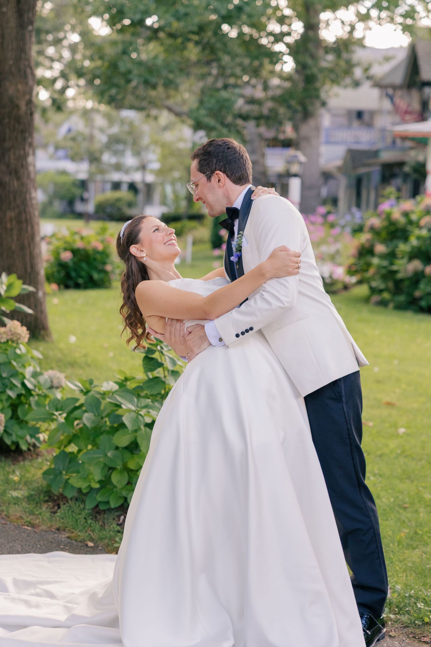 Bride and groom share a joyful dance embrace in a lush garden during their outdoor wedding celebration.