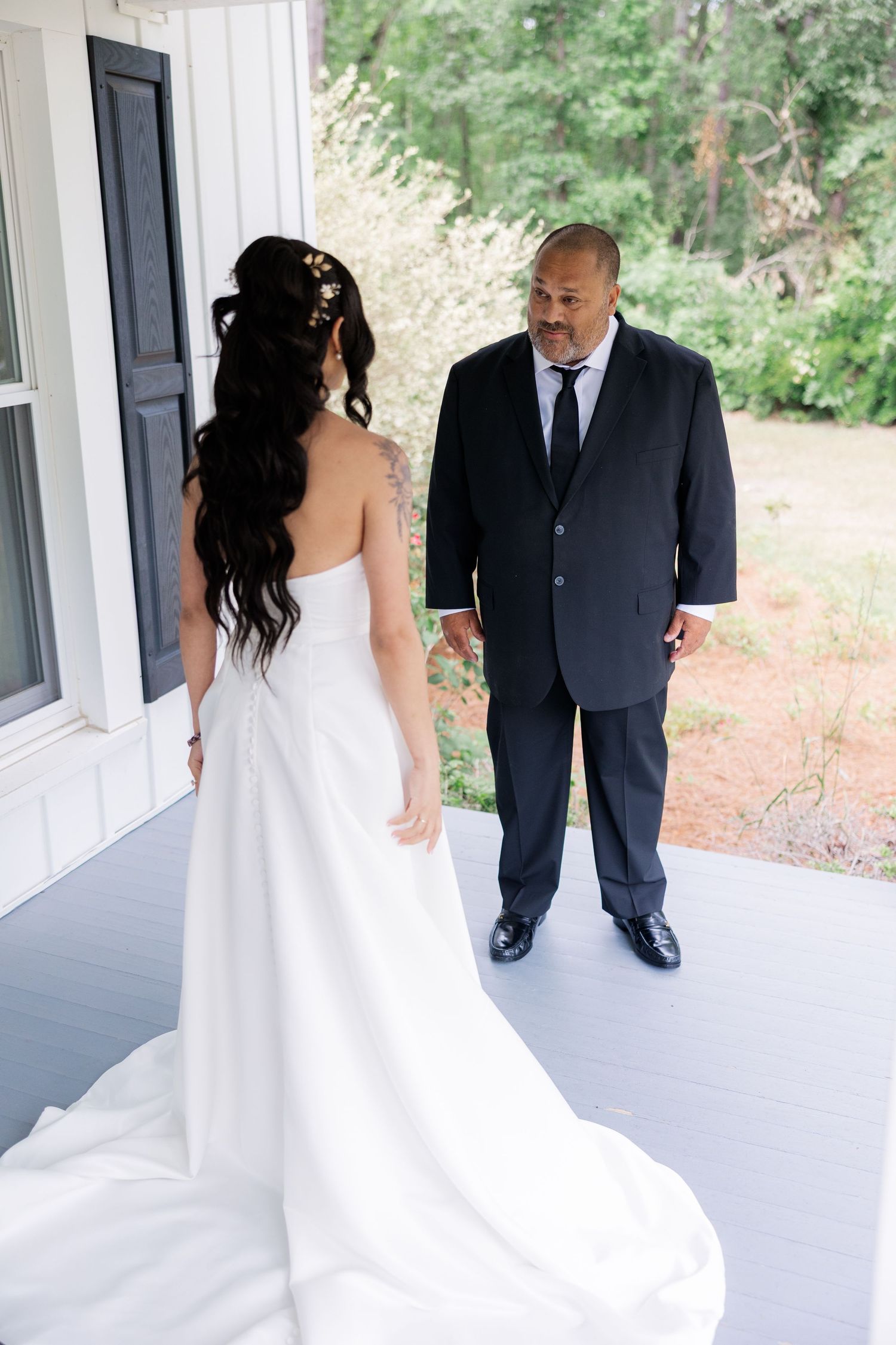 Elegant wedding dress train flowing on white porch with outdoor garden view.