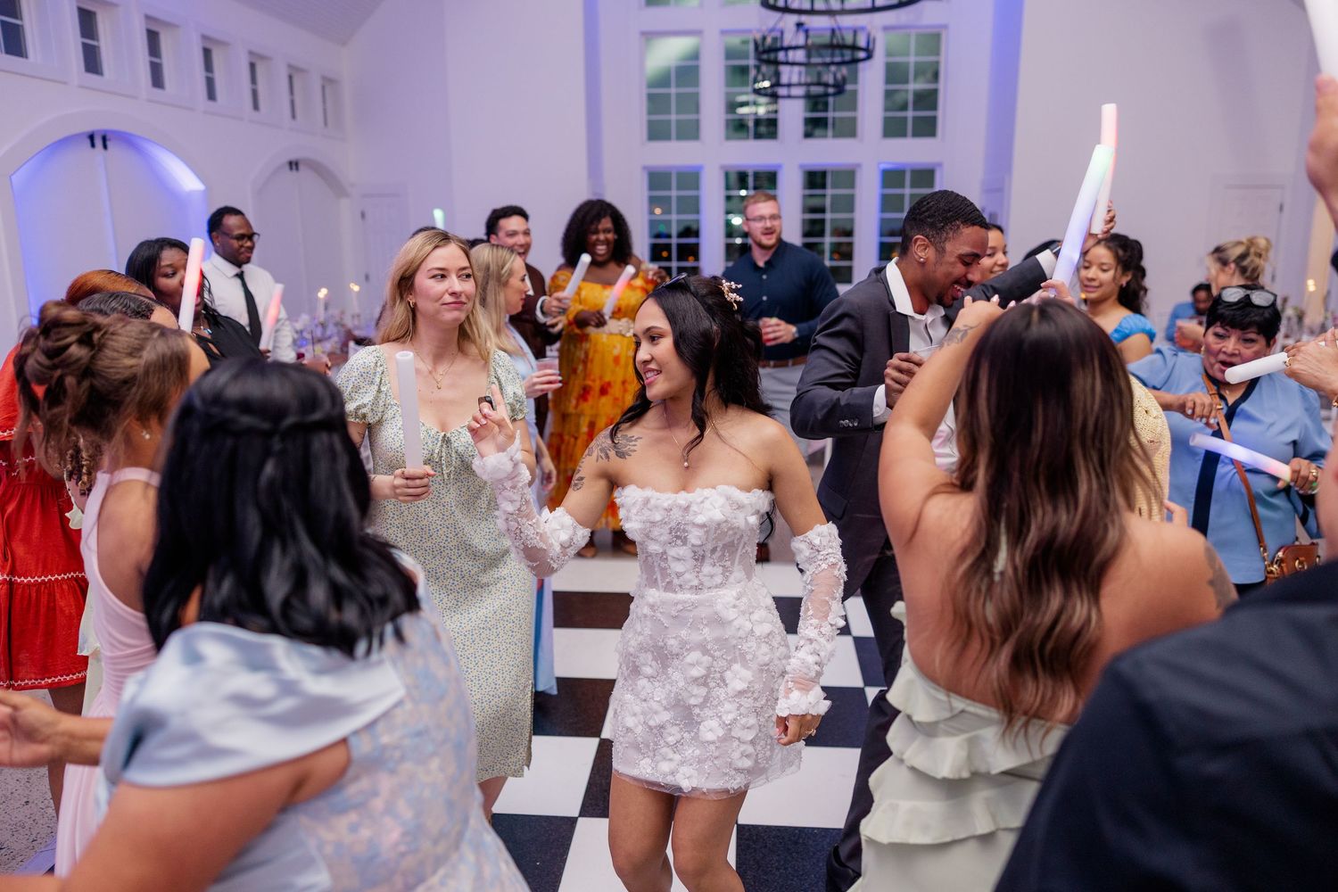Wedding guests dance and celebrate in reception venue with blue uplighting and white walls.