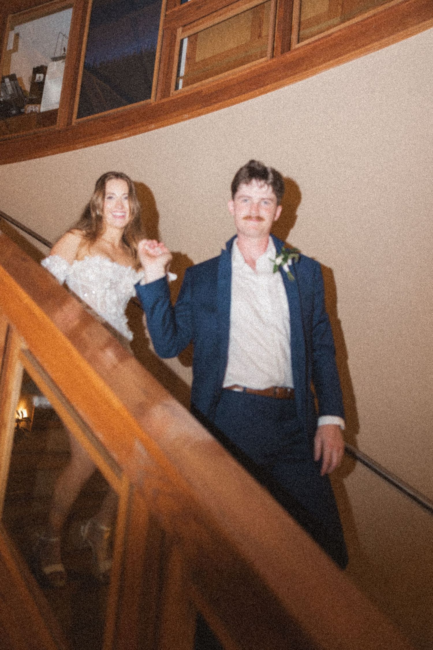 Newlyweds descending wooden staircase in formal wedding attire.