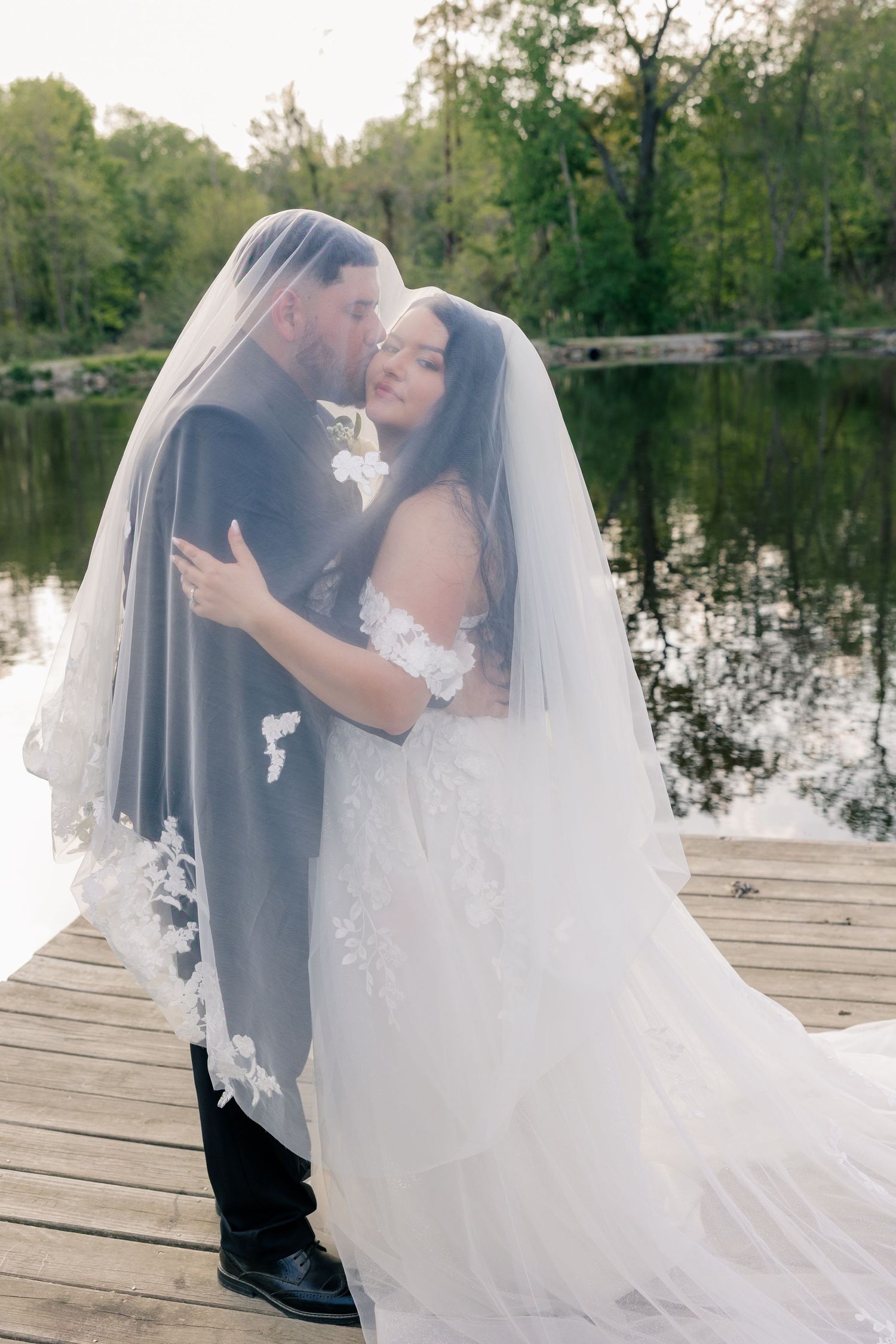 A romantic wedding couple shares intimate moments on a wooden dock by a serene lake during golden hour.