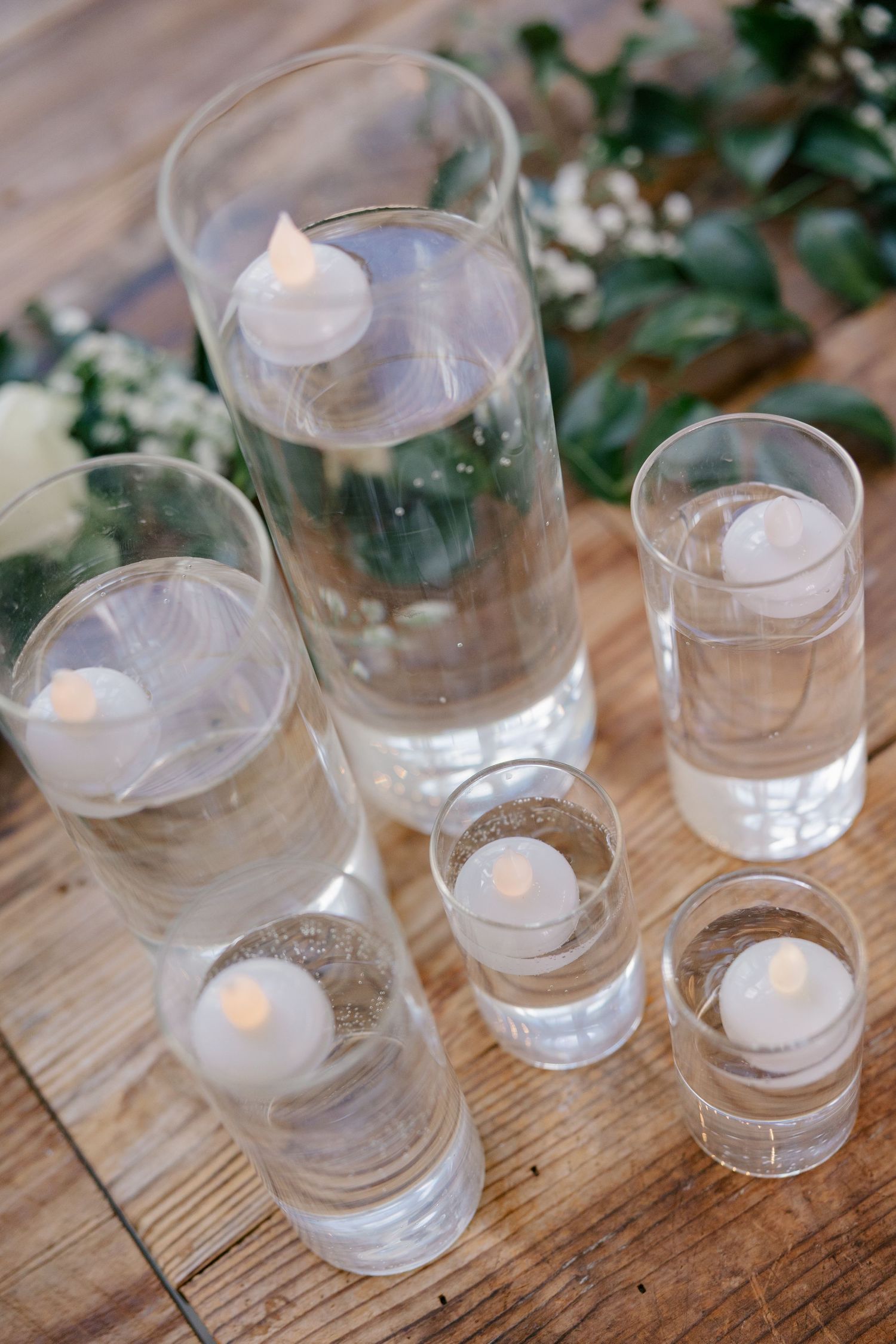 White tea light candles arranged in clear glass holders on a rustic wooden surface.