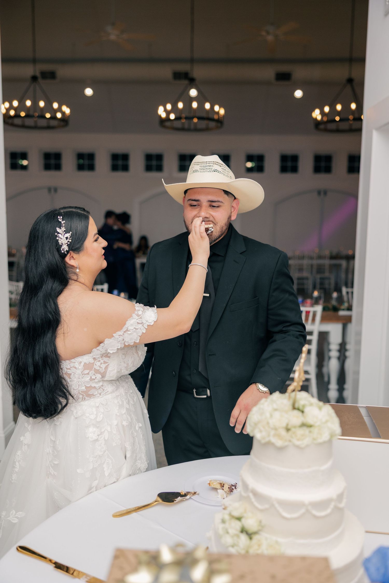 Newlyweds share cake cutting moment at reception with white floral decor.