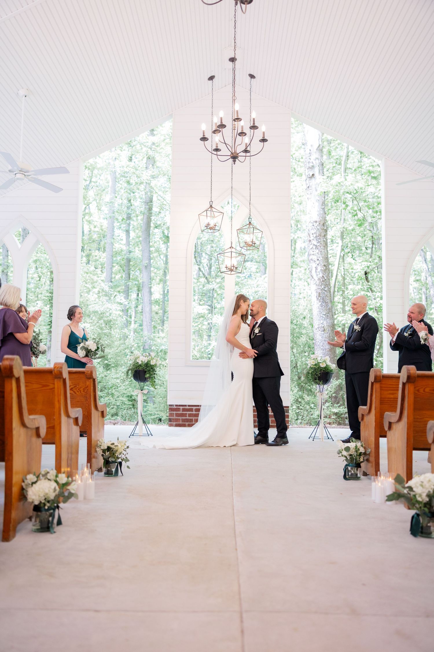 Light-filled chapel interior with wooden pews and floral decorations during a wedding ceremony.