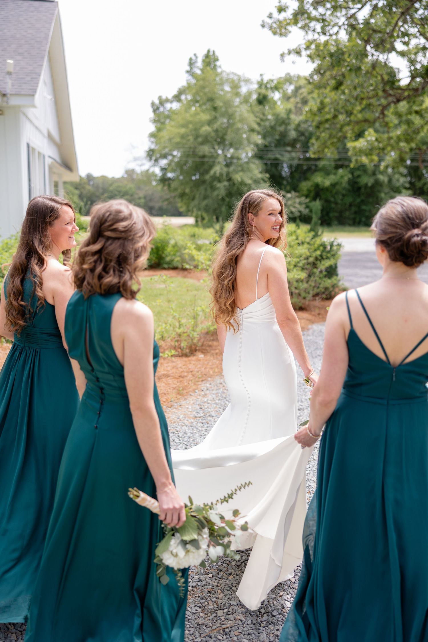 Bridal party in teal dresses walk together outside white chapel venue.