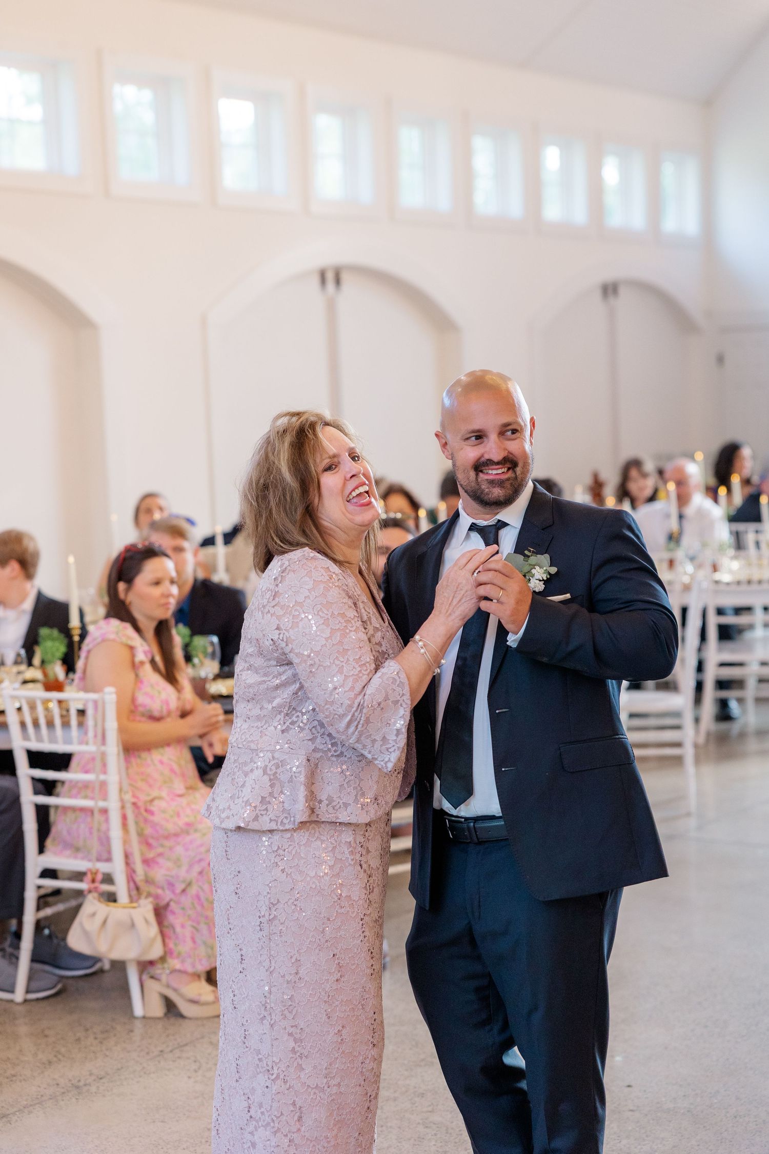 Wedding reception dance scene in bright white venue with guests celebrating.