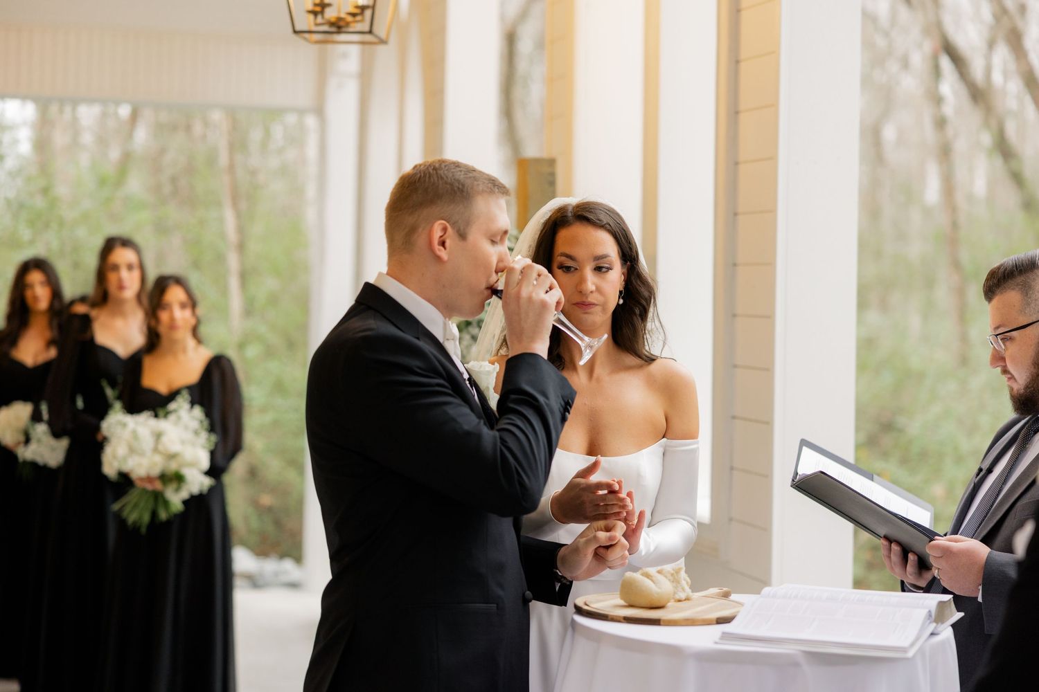 An elegant wedding ceremony taking place in a bright white chapel with guests looking on.