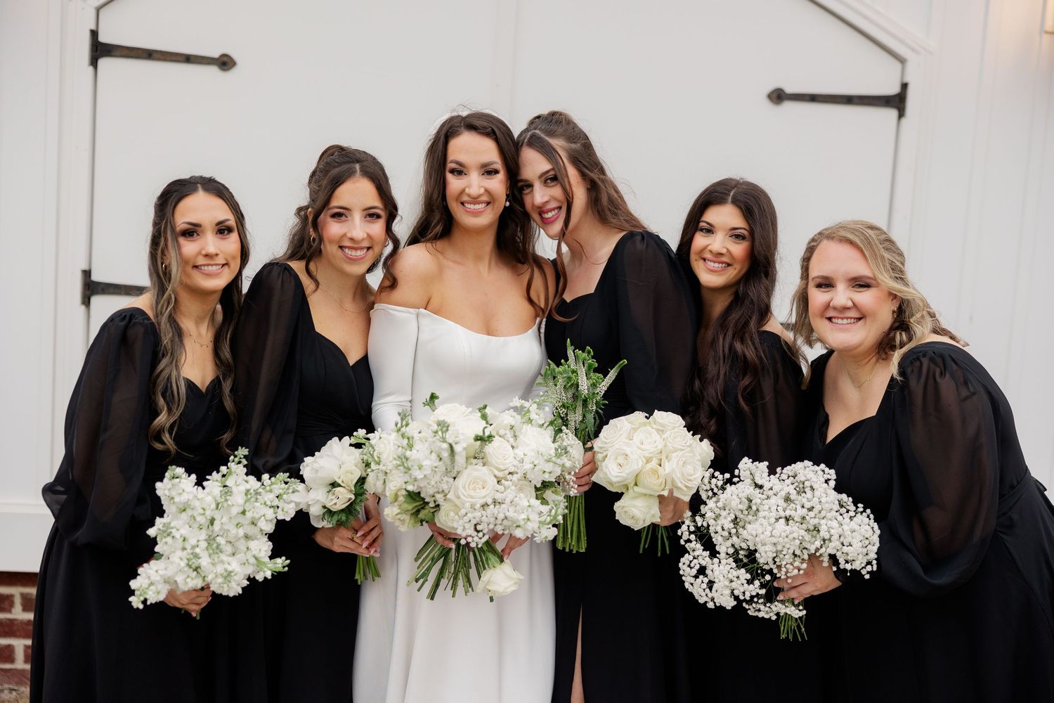 Wedding party in black dresses posing with white floral bouquets.