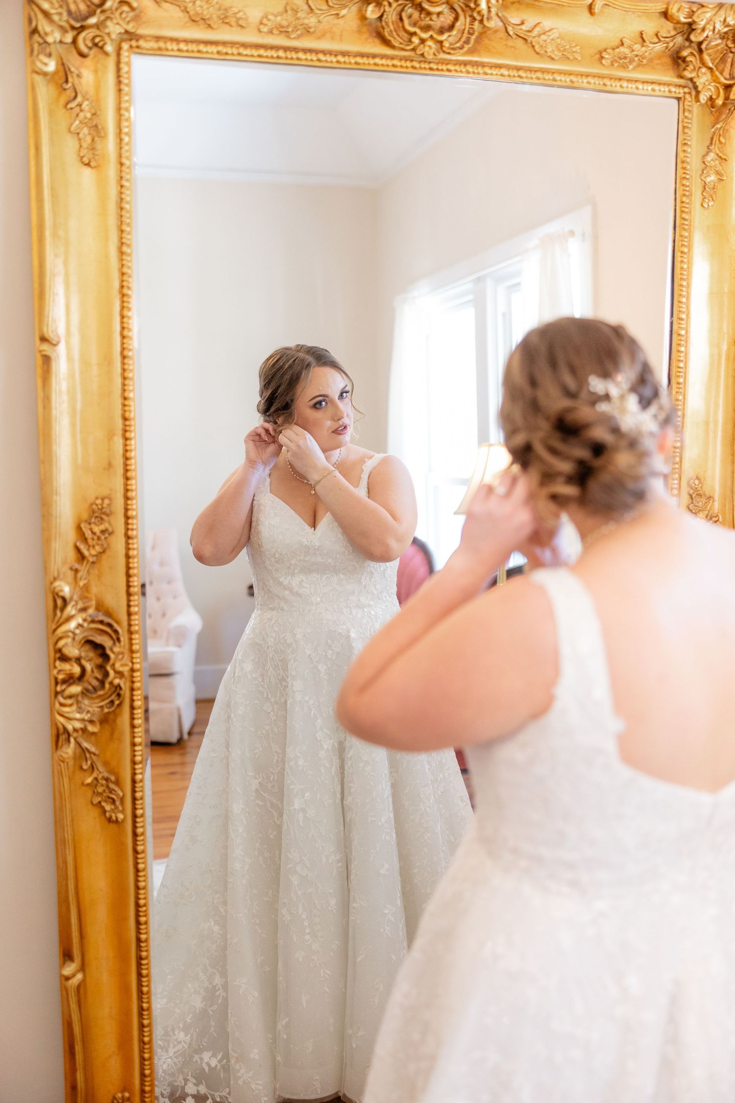 Bride gets ready in an elegant room with an ornate gold-framed mirror.