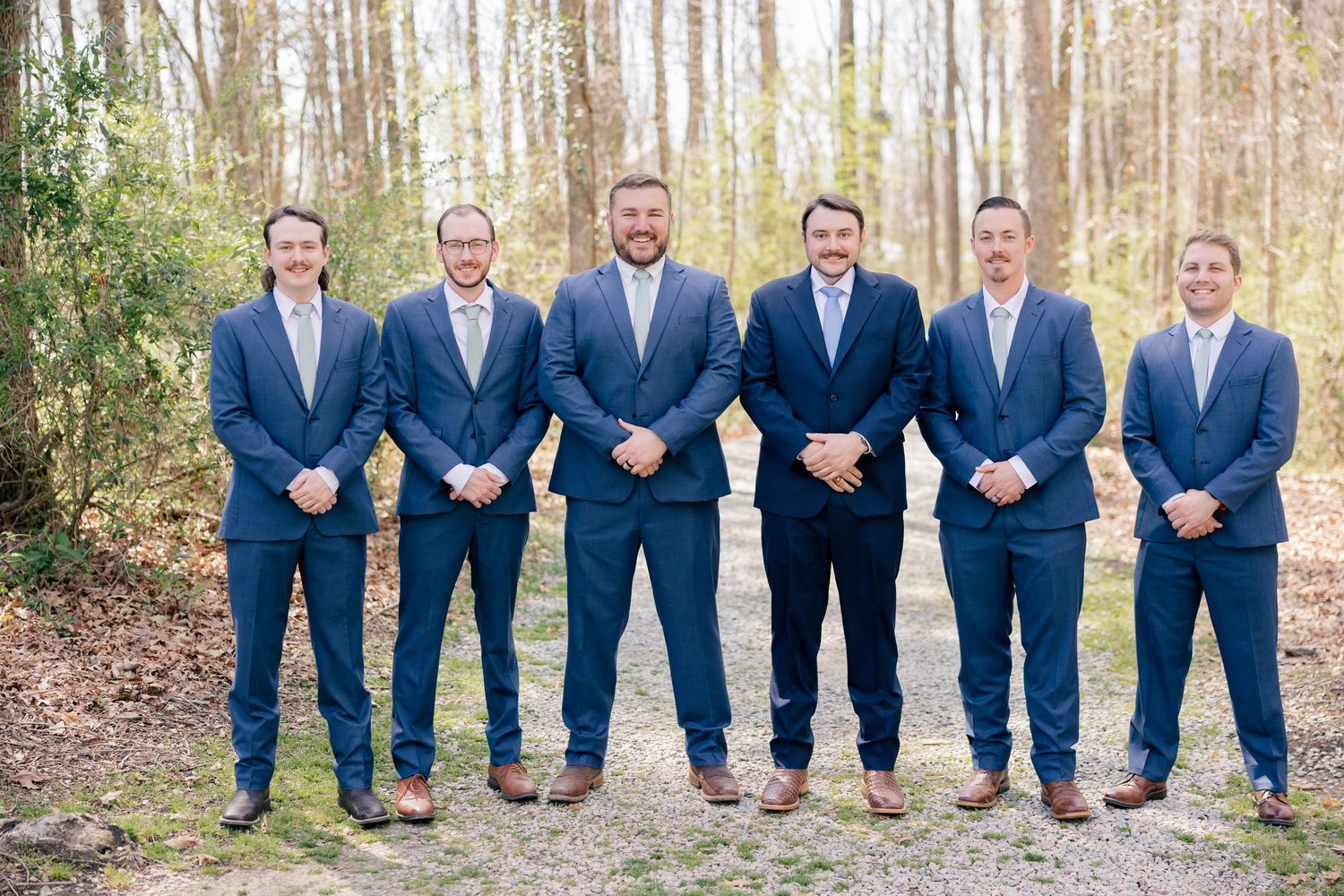 Groomsmen wearing matching navy suits showing off colorful socks while kneeling outdoors.