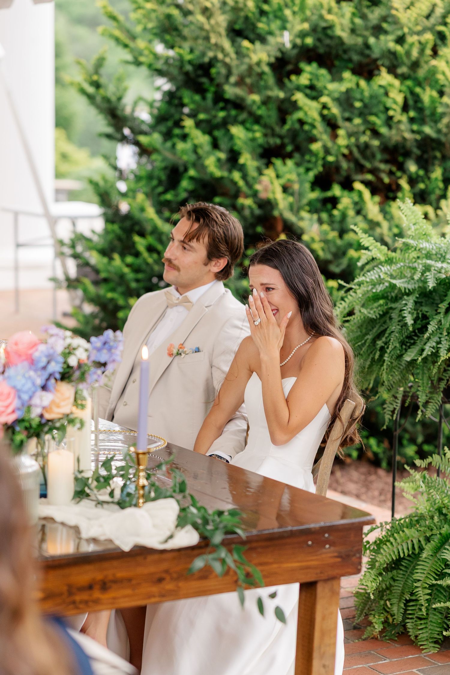 Couple laughing together at wooden table during outdoor wedding reception.