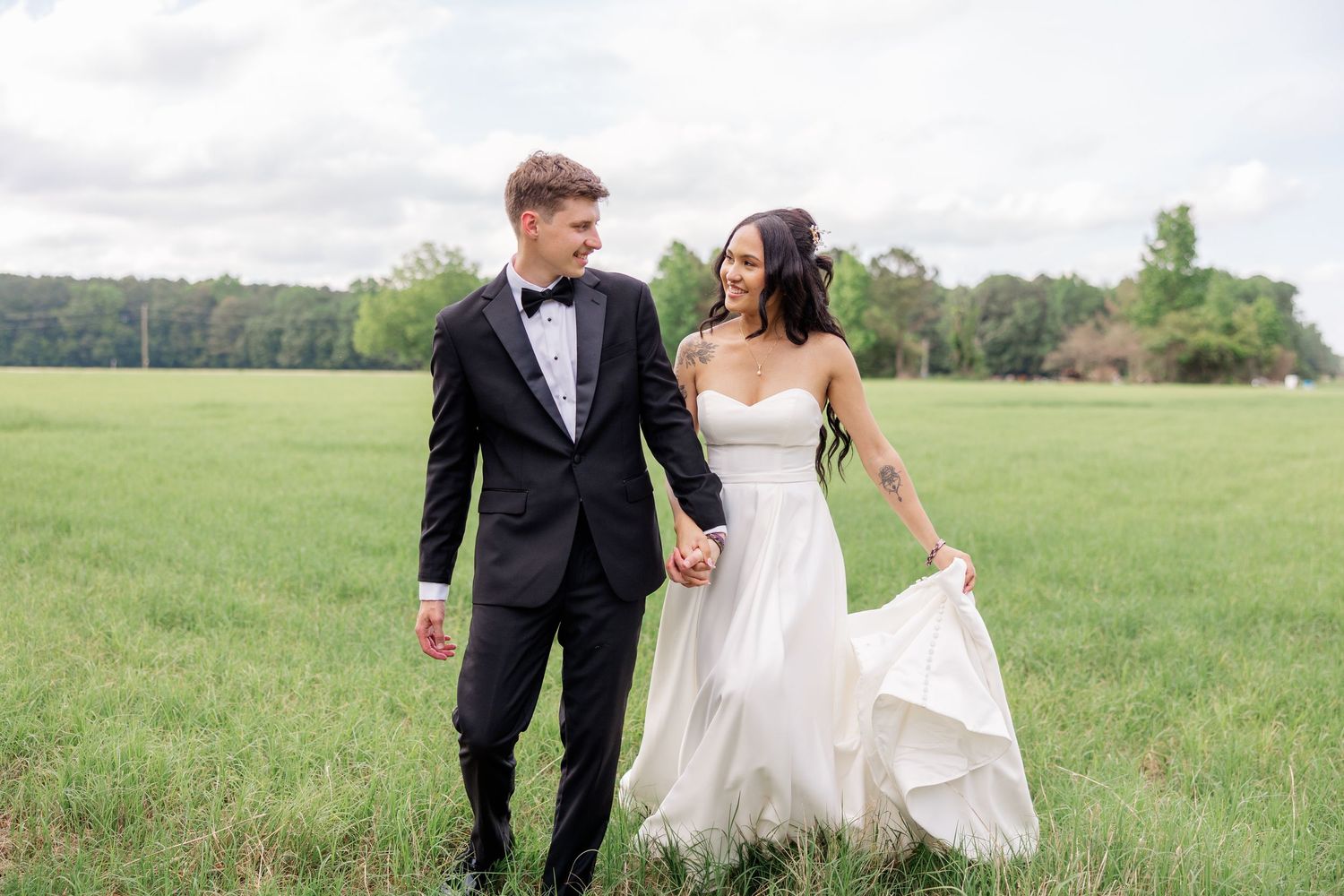 Newlyweds share candid moments while walking through sunny green meadow.
