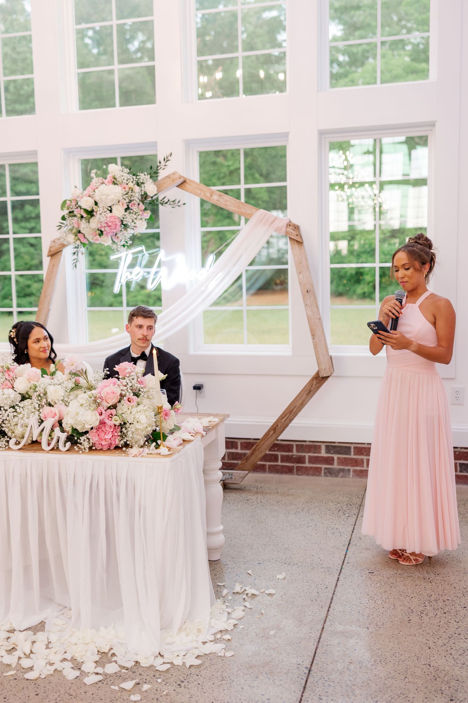 Wedding reception setup with floral arch and speaker giving toast.