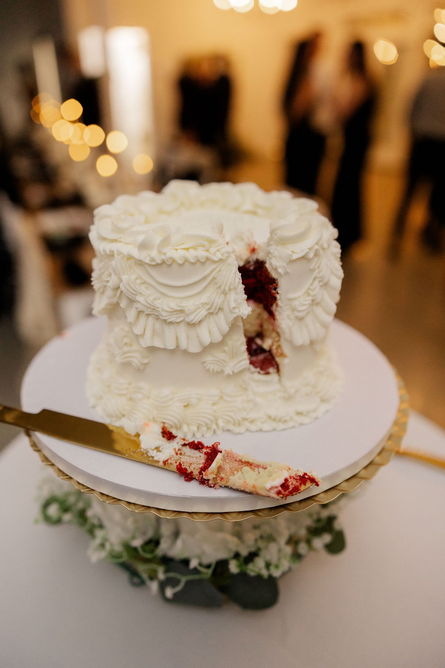 A white wedding cake with ruffled frosting details and red velvet layers being served.