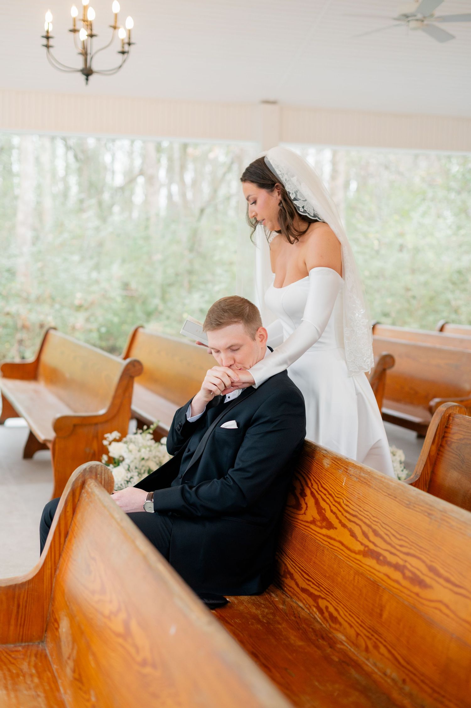 A tender moment between newlyweds in a church pew surrounded by natural light.
