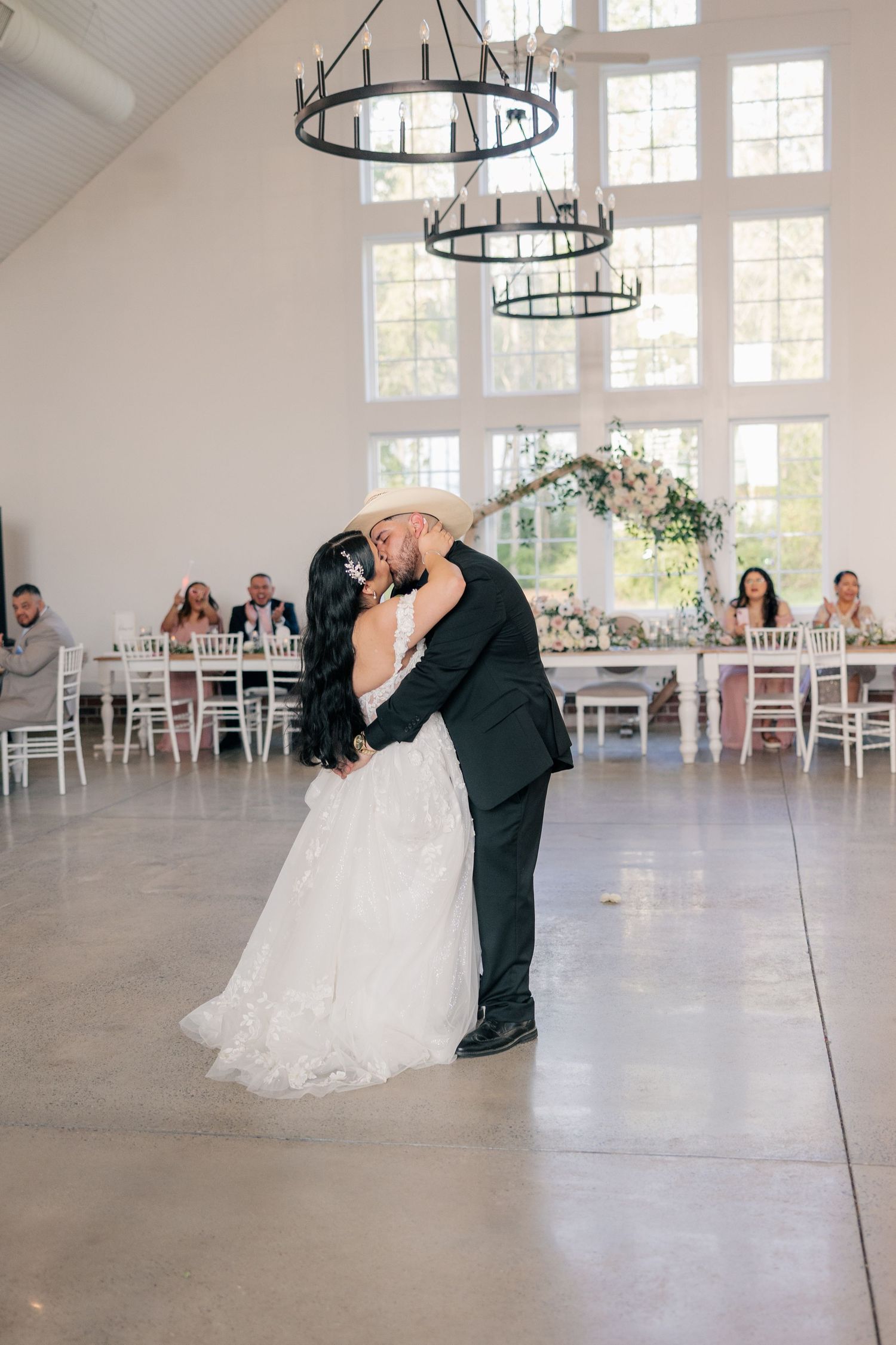 Elegant wedding dance dip pose in a modern white reception hall with chandeliers.