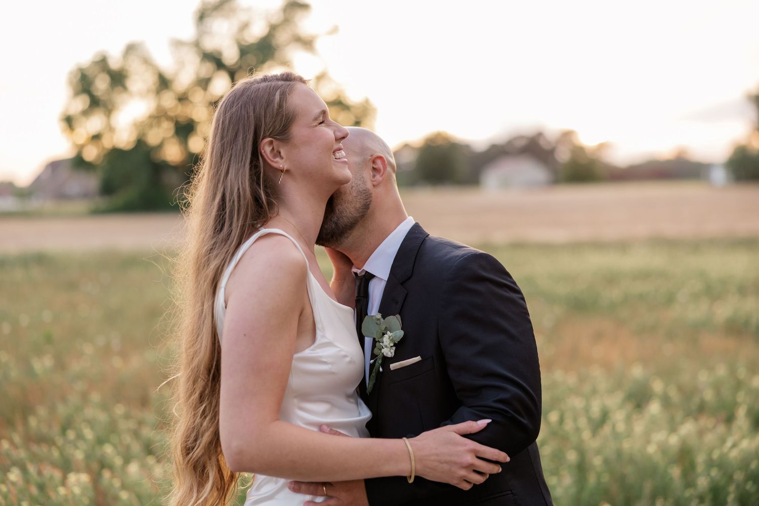 A romantic wedding couple embracing in a sunlit meadow during golden hour.
