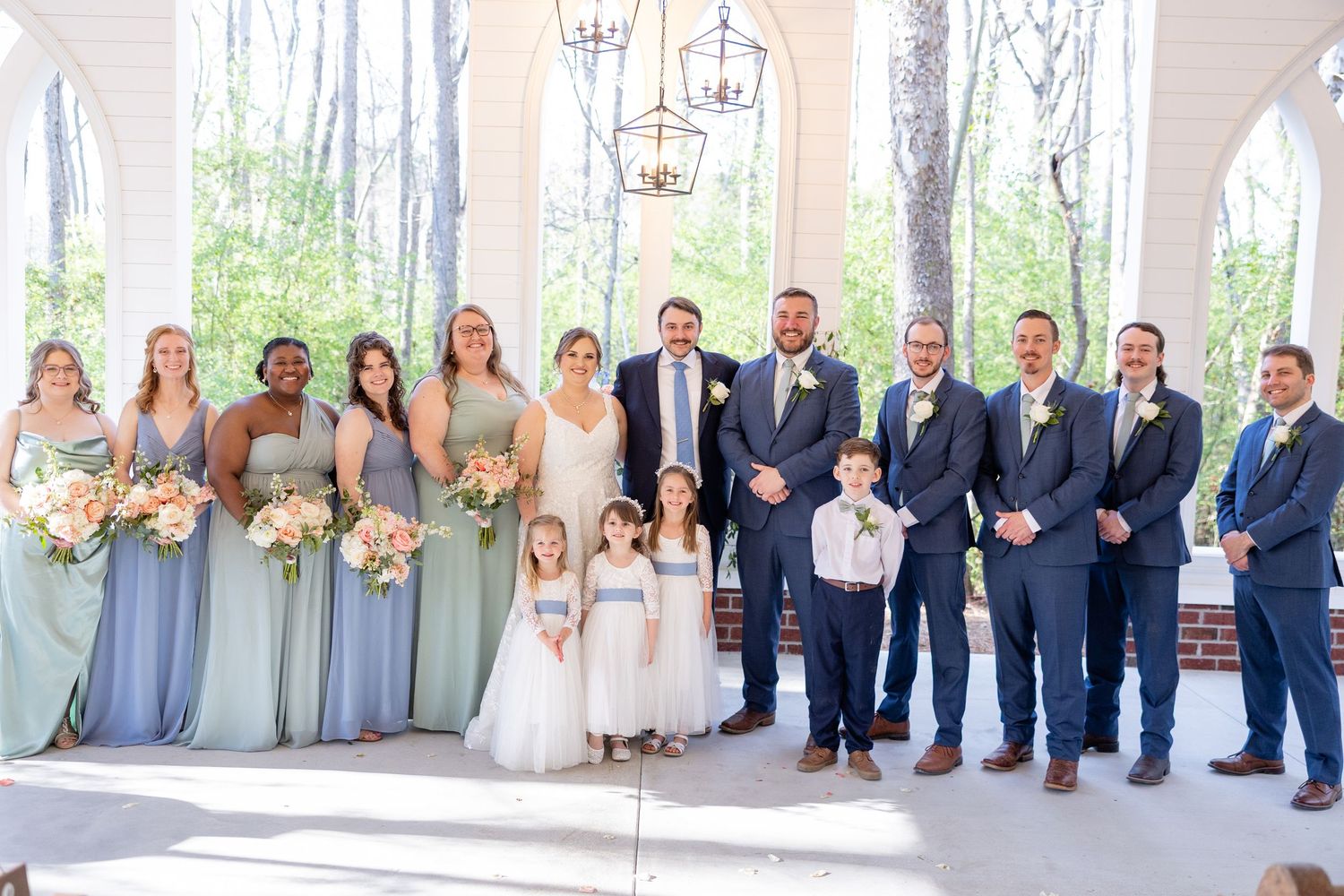 Wedding party lineup with bridesmaids in blue dresses and groomsmen in navy suits.