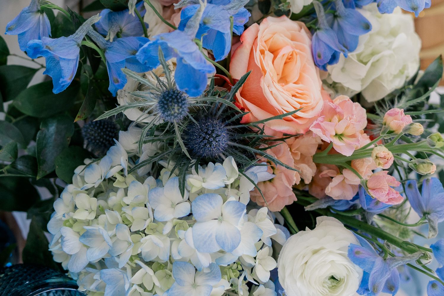 Wedding bouquet featuring blue delphiniums, peach roses, and white hydrangeas.