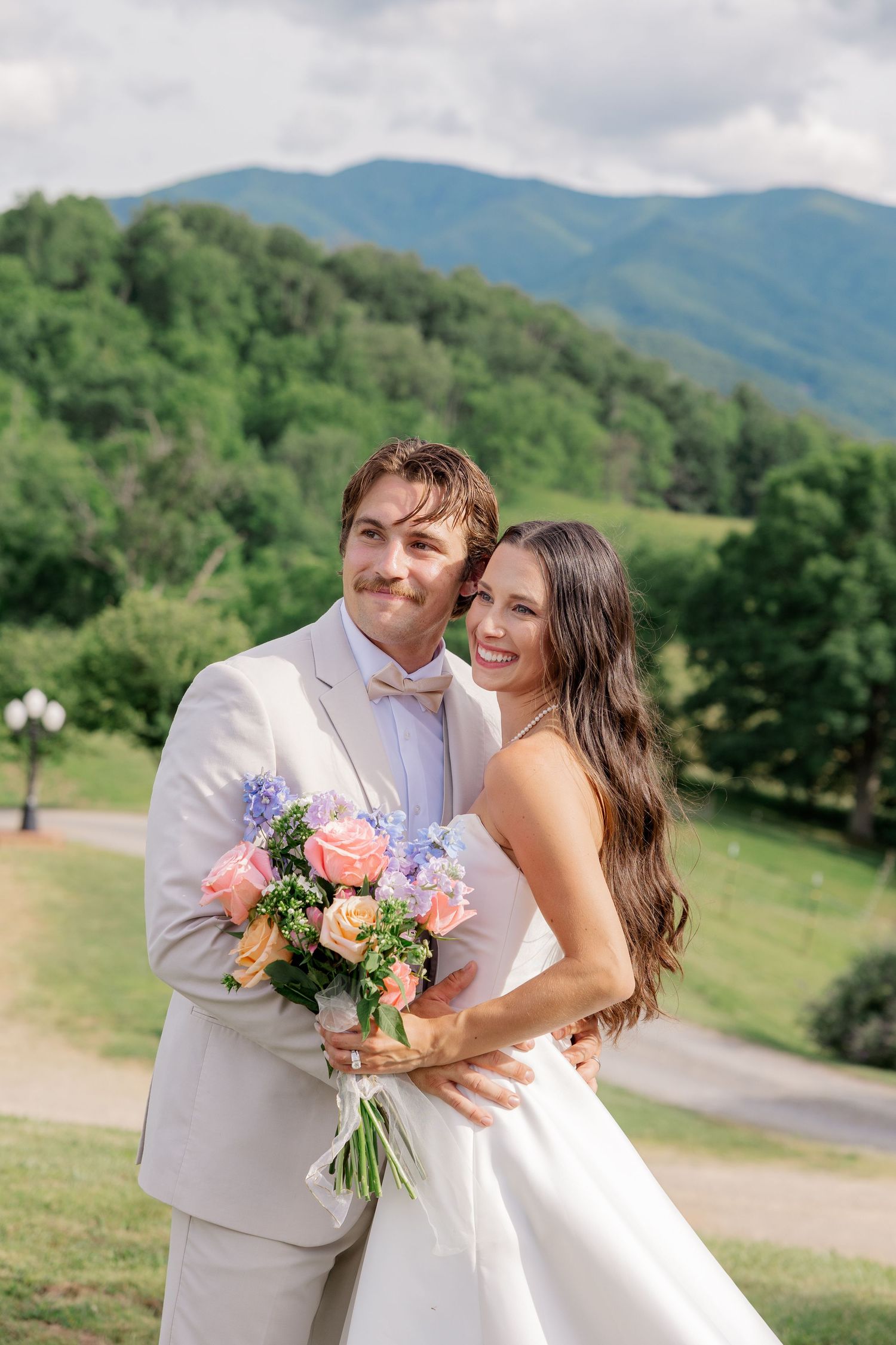 A couple embraces on their wedding day with mountains and green trees in the background.