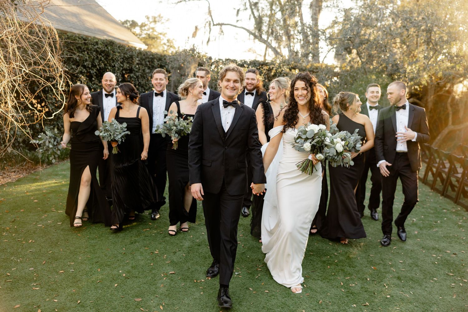 A wedding party walks together on a lawn during golden hour celebrations.