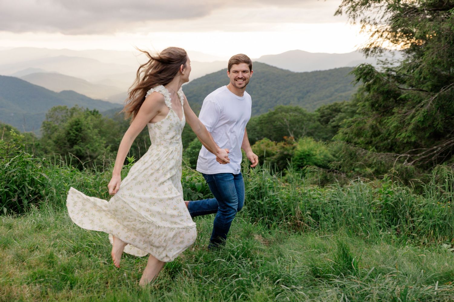A couple frolics in a mountain field, with one person wearing a flowing white dress.