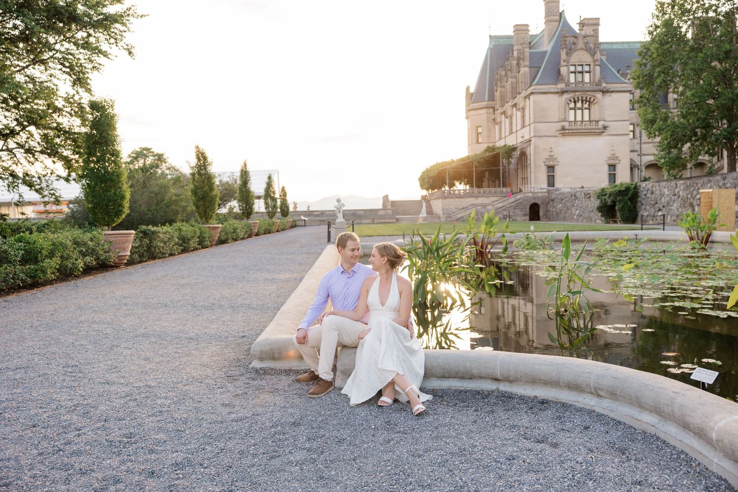 Romantic wedding couple walks through scenic European castle grounds during golden hour sunset.