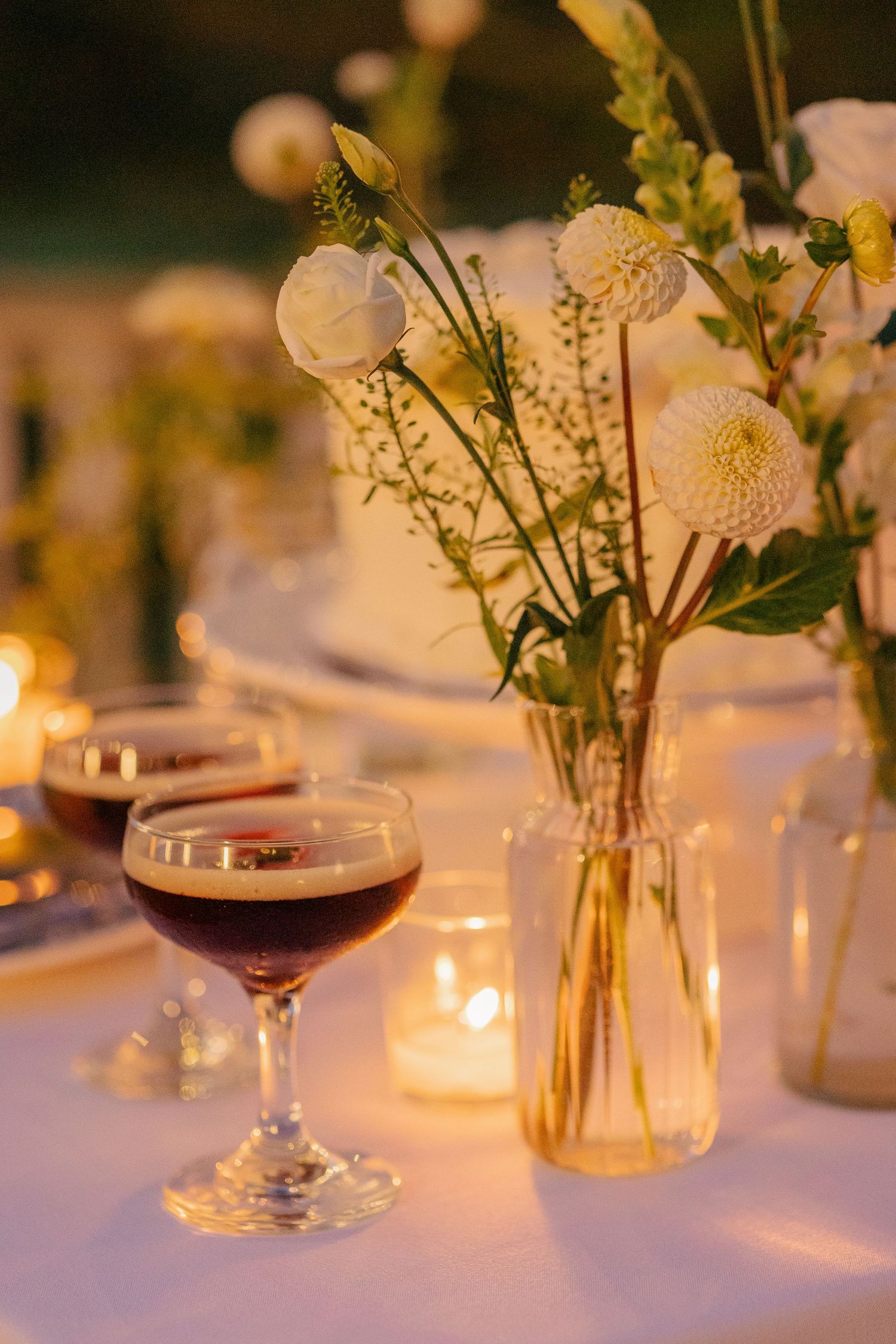 Elegant wedding reception table with espresso martinis, white dahlias, and glowing candles at dusk.