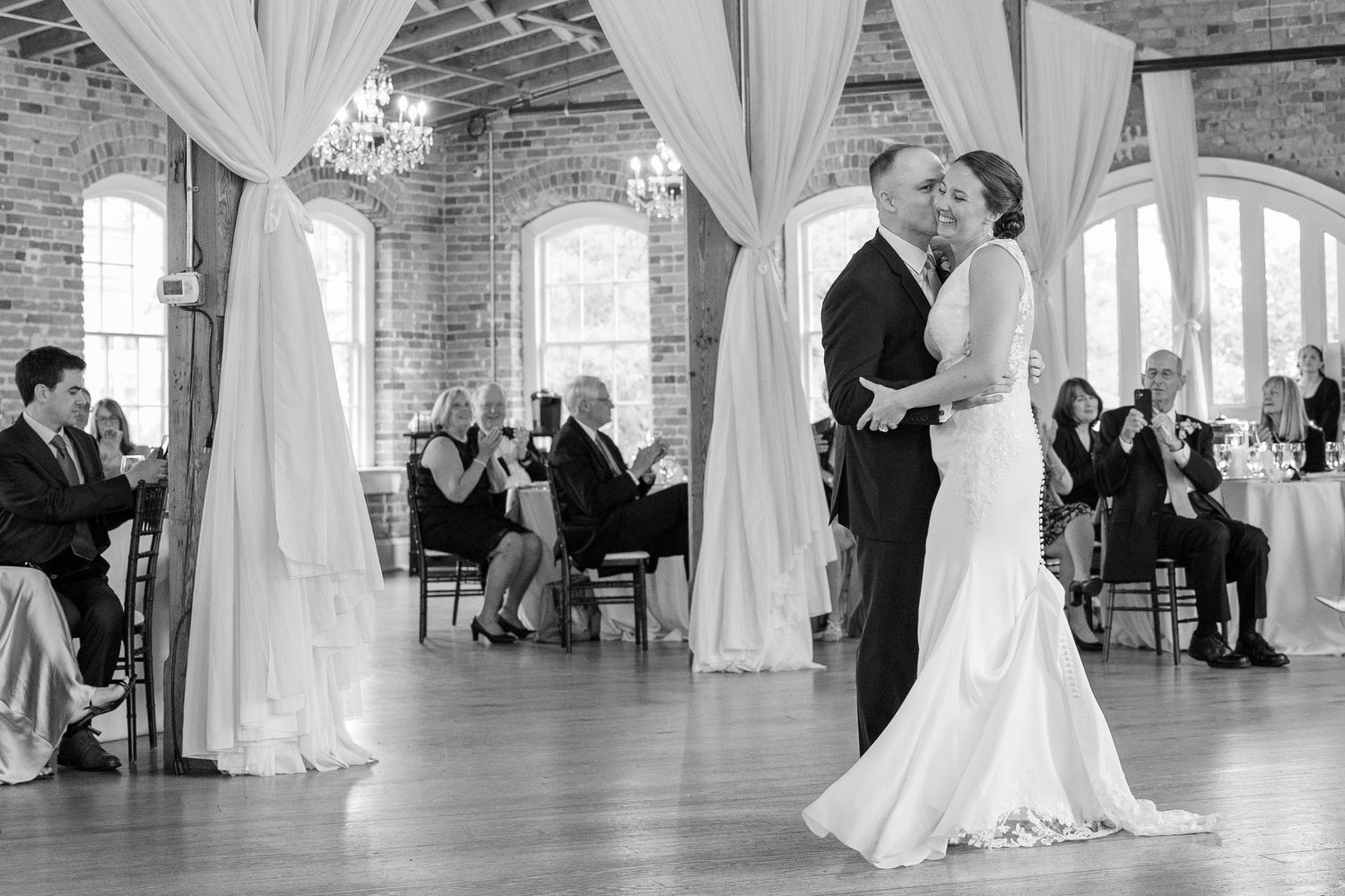 Bride and groom share their first dance in a black and white photo at an elegant brick venue.
