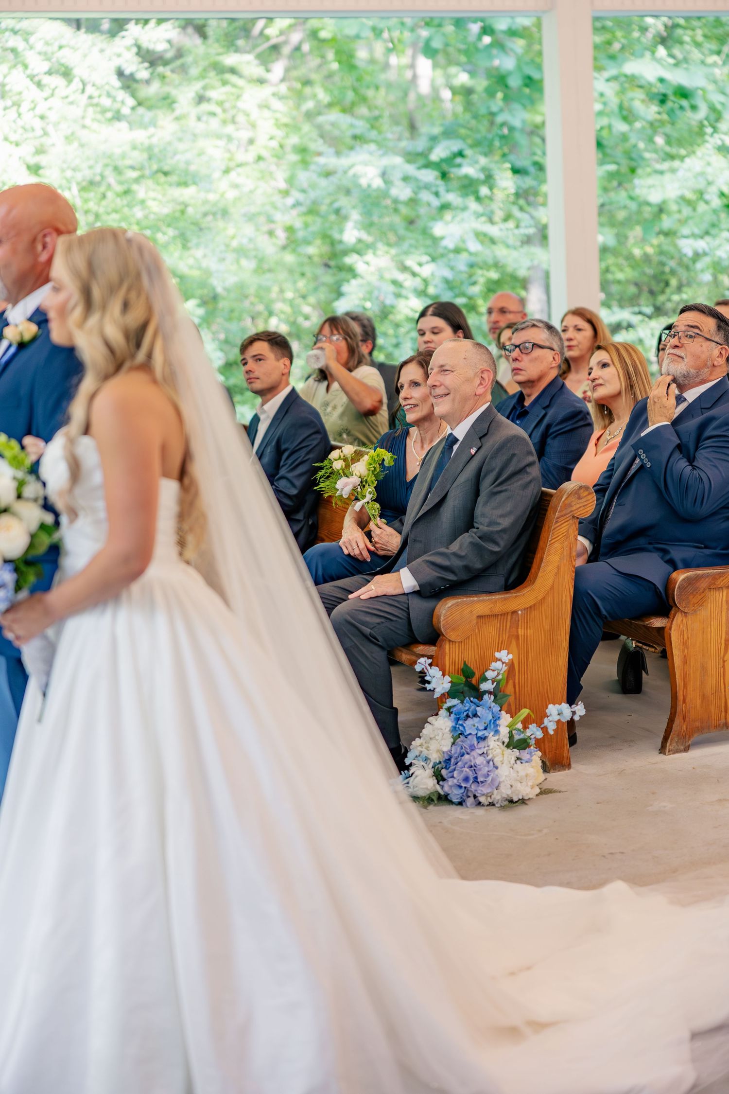 Bride walking down the aisle in a white gown as smiling guests watch the wedding ceremony.