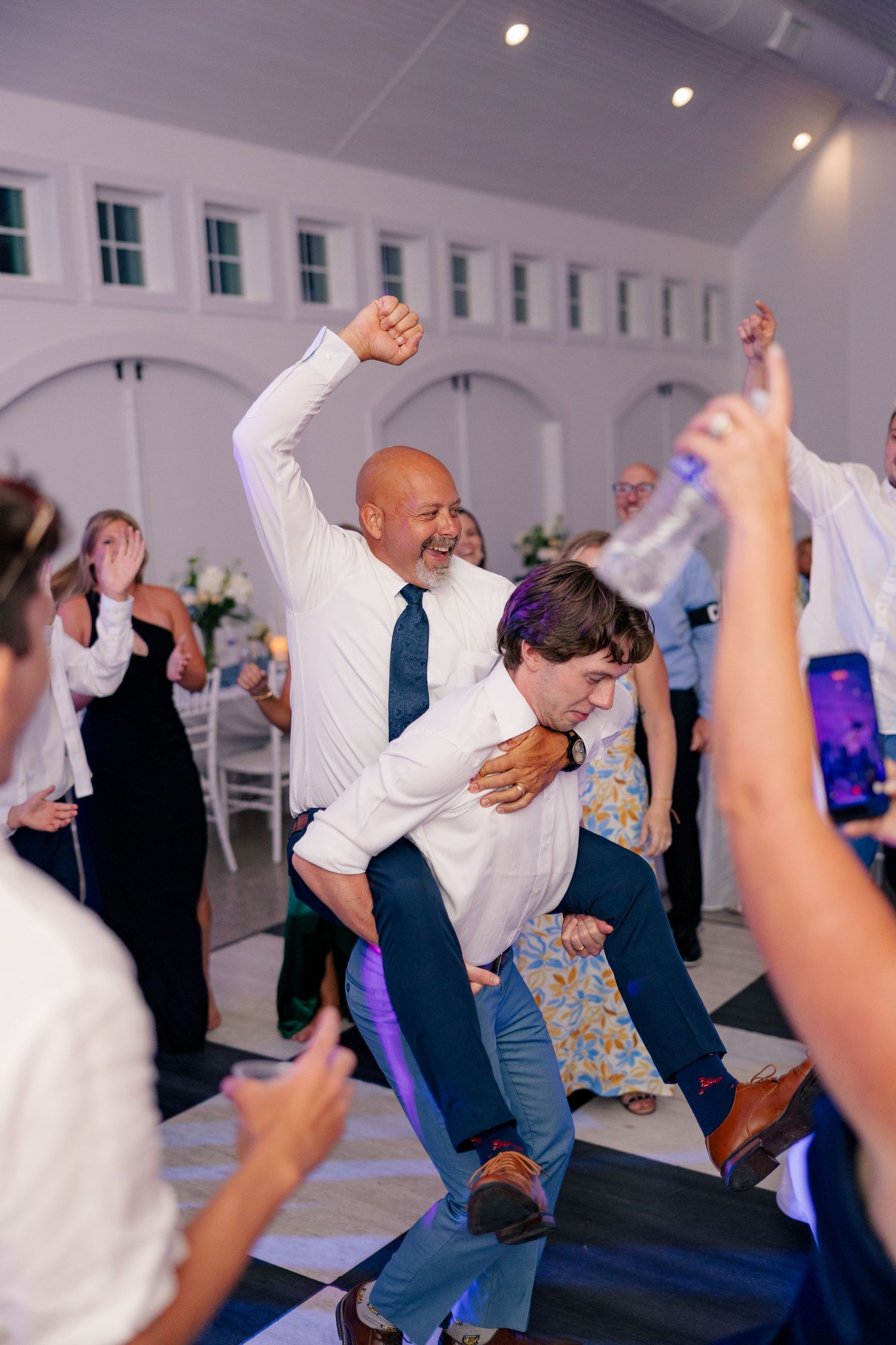 Joyful wedding guest riding piggyback on the dance floor during lively reception.