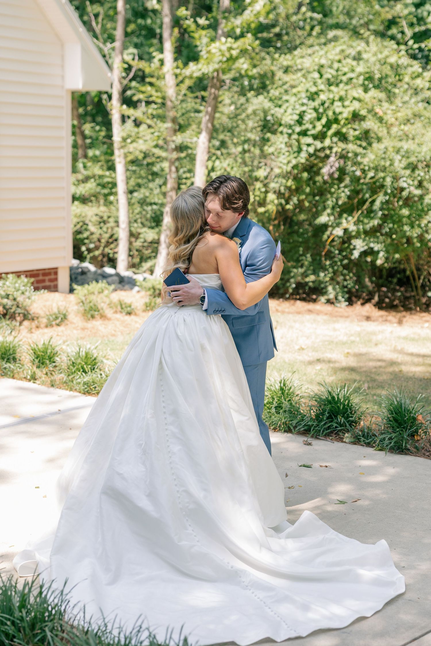 Bride and groom embrace tenderly during outdoor first look at wedding venue.