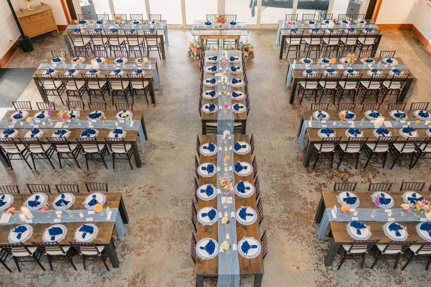 Aerial view of wedding reception hall with long wooden tables set with navy blue napkins and florals.