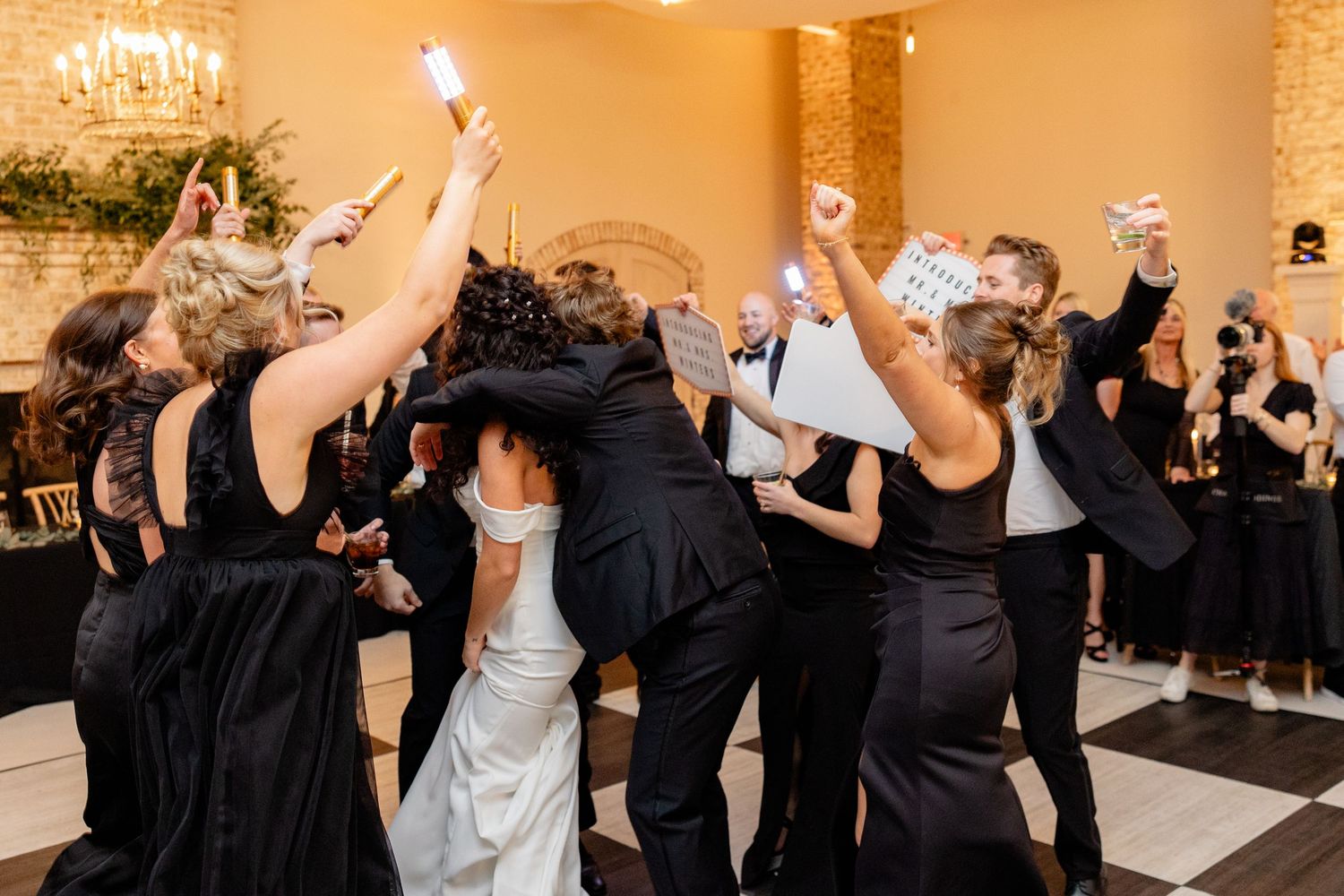 Wedding party dancing and celebrating with raised arms on black and white checkered dance floor.