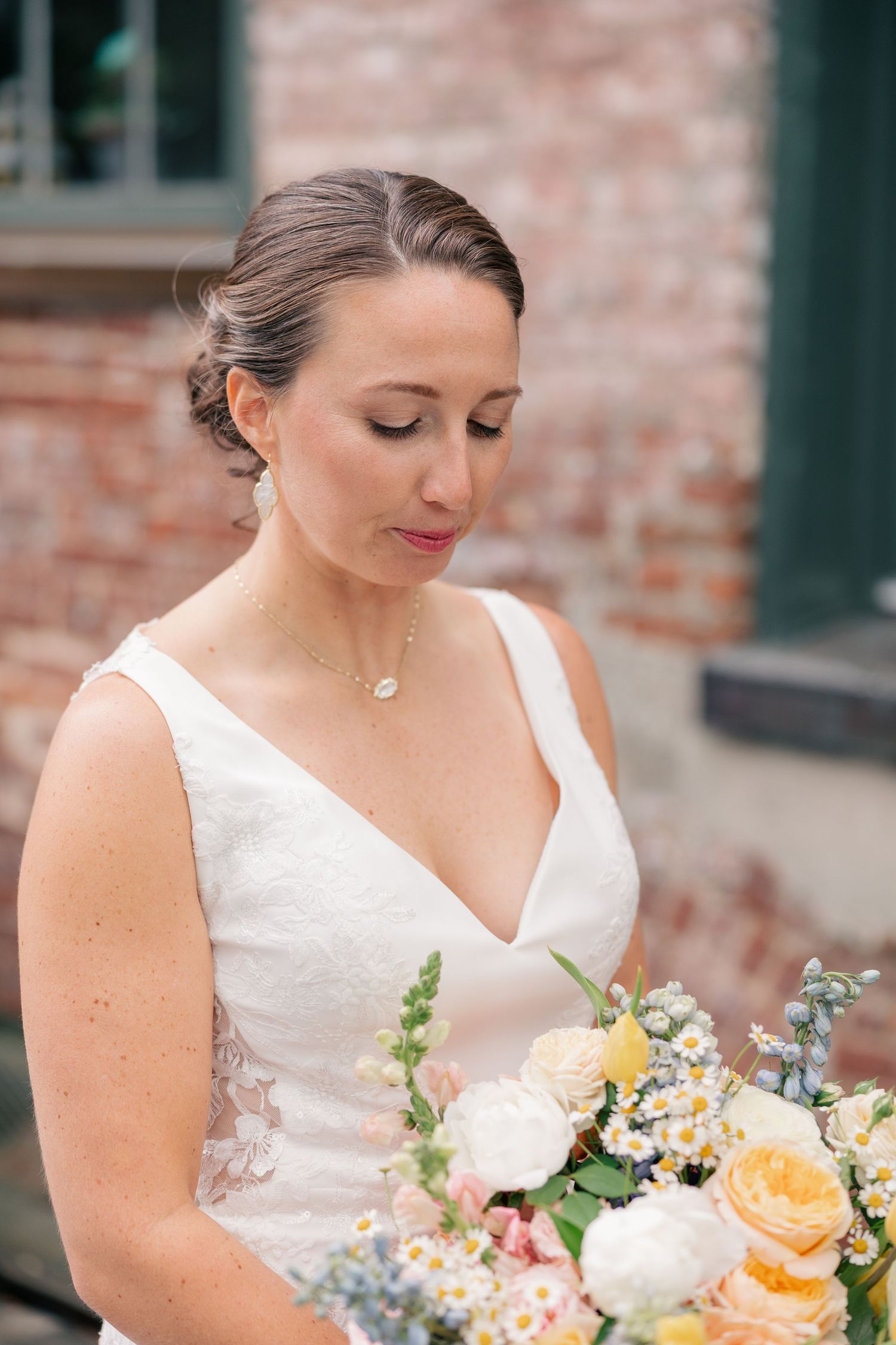 Beautiful bride in a V-neck lace wedding dress holding a colorful spring bouquet outdoors.