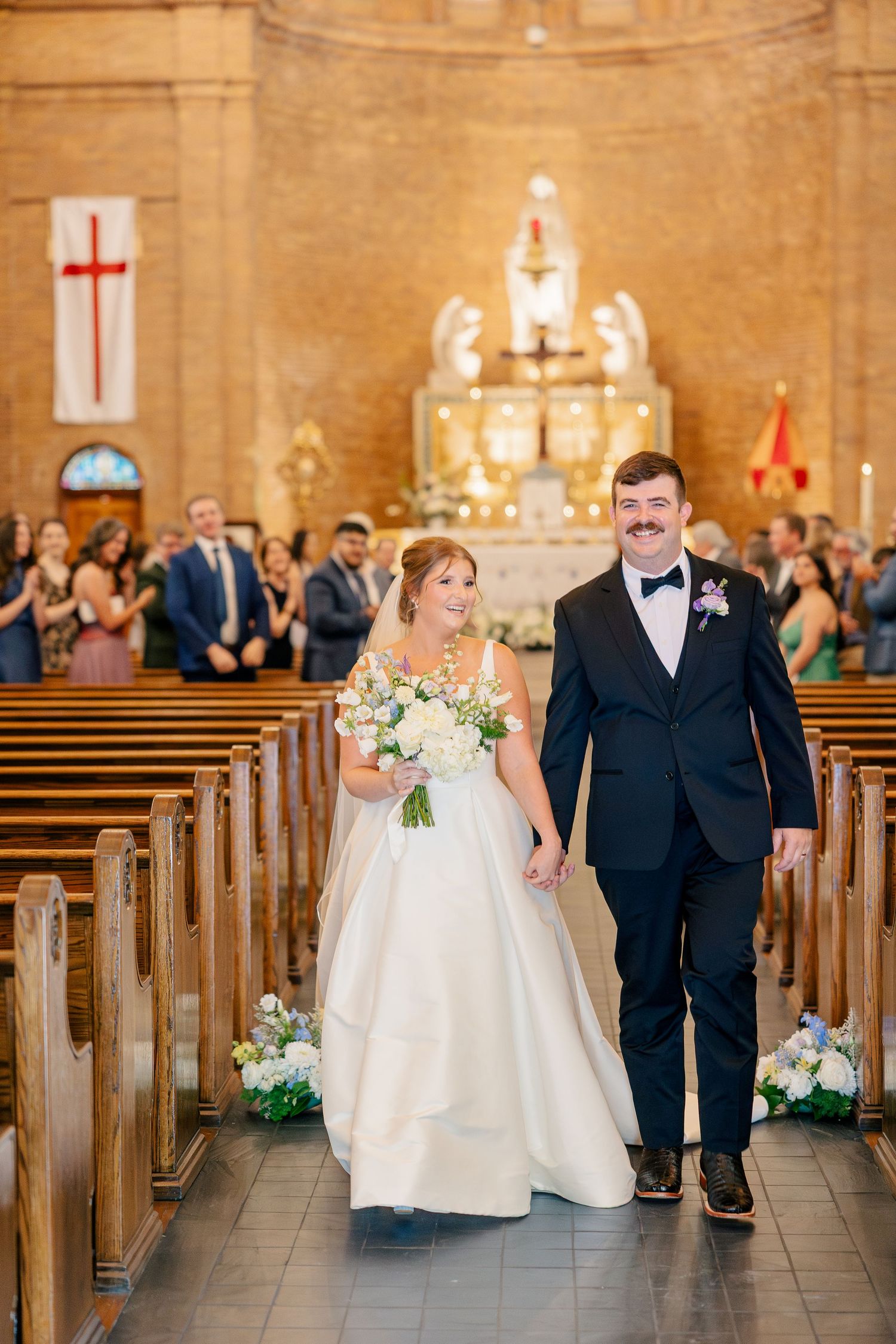 Newlyweds walk hand-in-hand down the church aisle after their wedding ceremony, bride holding bouquet.