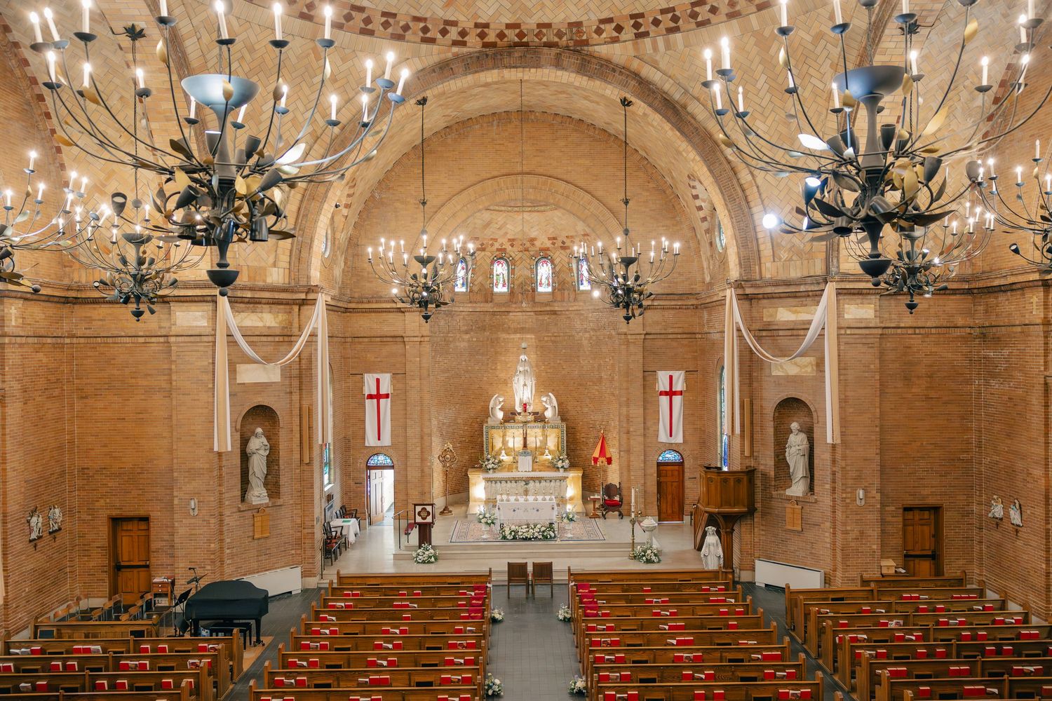 Grand brick church interior with ornate chandeliers, wooden pews, and decorated altar.