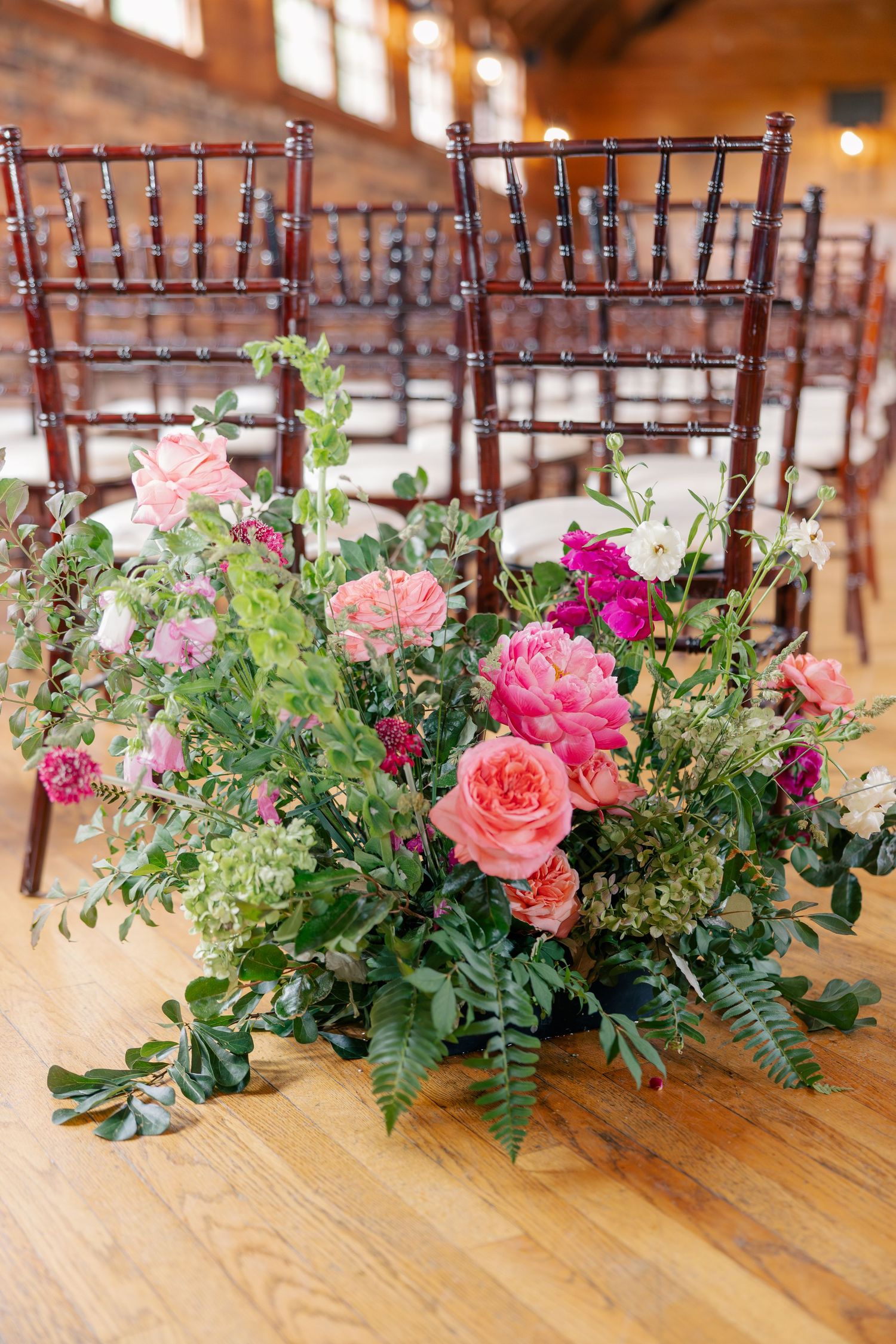 Lush pink and green floral centerpiece arrangement on wooden floor at wedding reception.