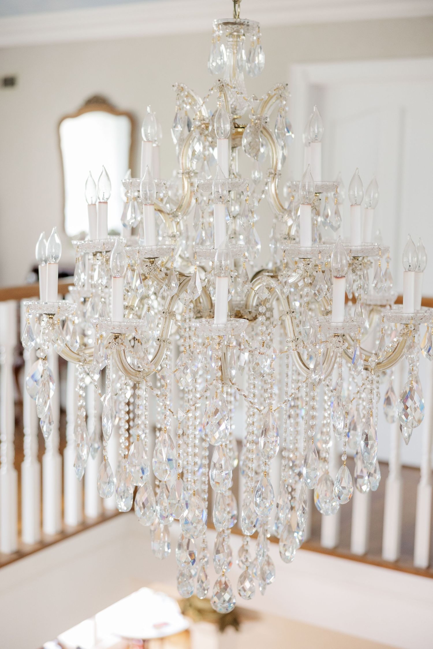 An elegant crystal chandelier with multiple tiers of sparkling glass drops hangs in a bright white room.