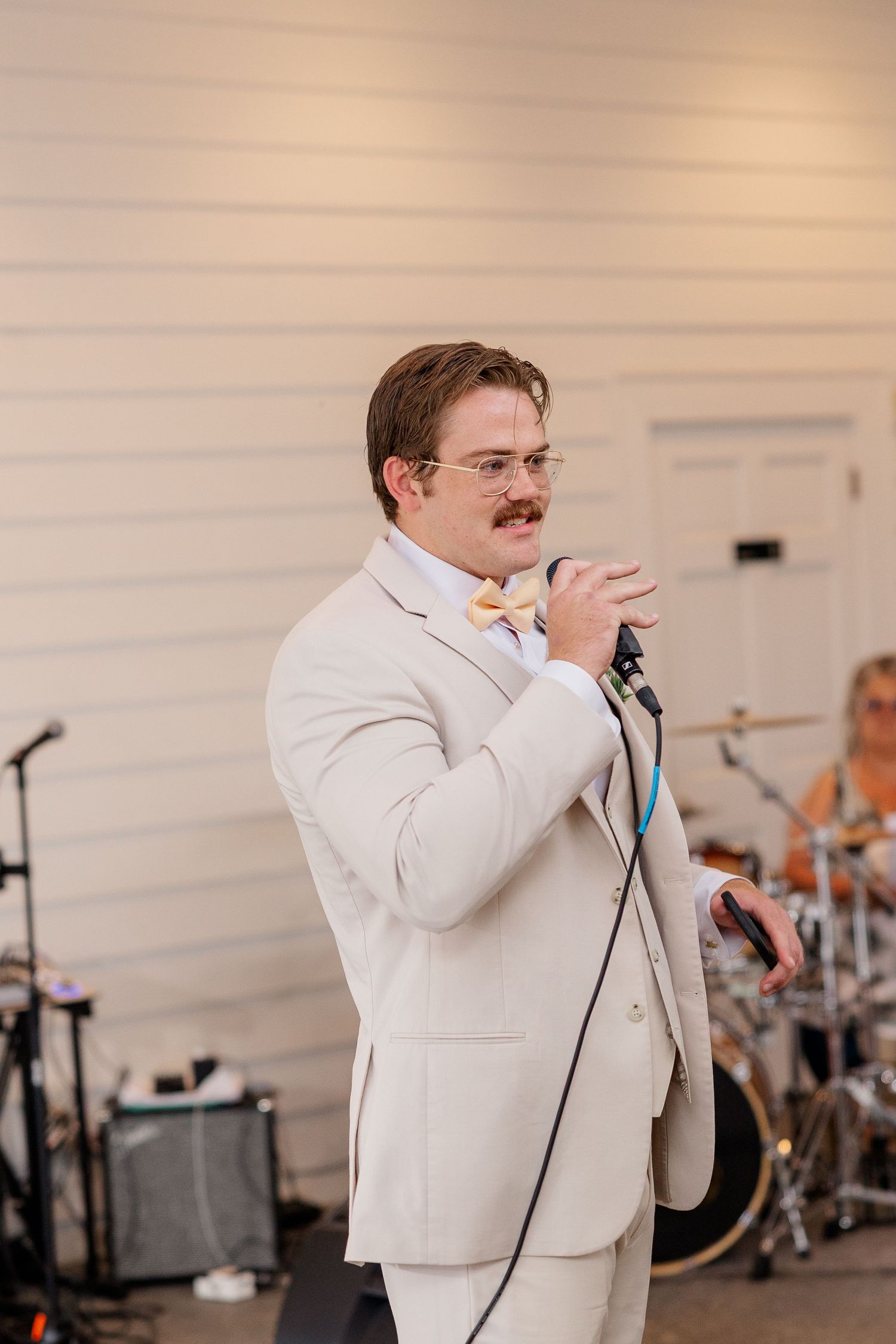 A performer in a white suit singing emotionally into a microphone during a wedding reception.