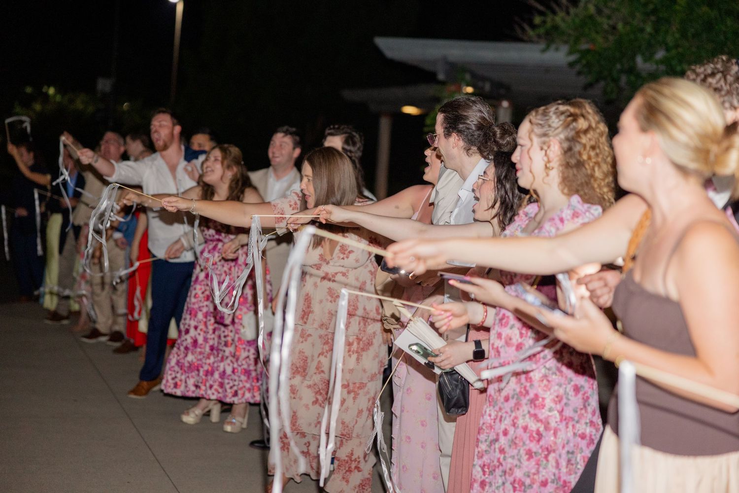 Wedding guests form a celebratory line during an outdoor reception.